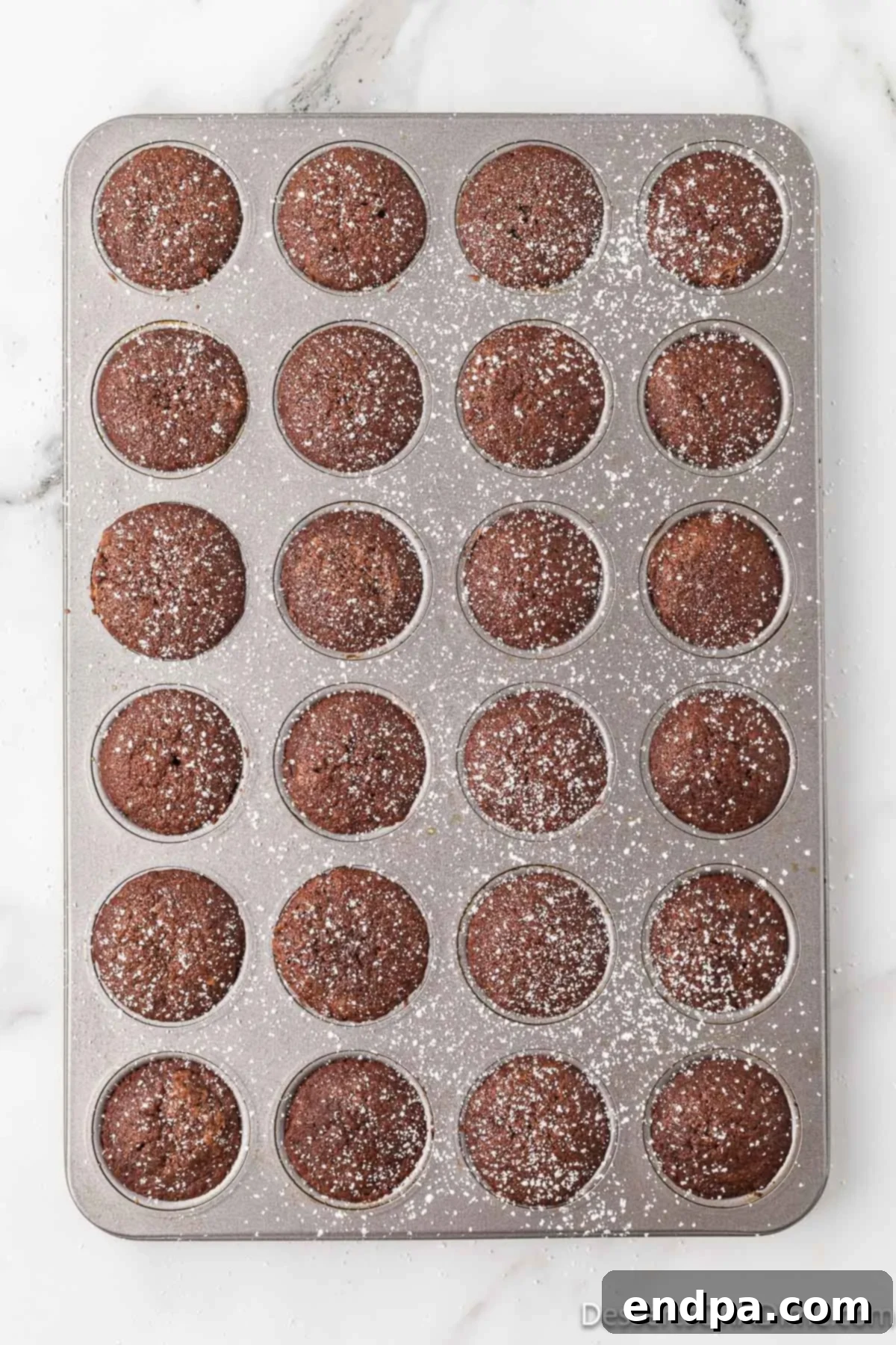 Bite-Sized Brownie Delights 5 Freshly baked mini brownies cooling on a wire rack, with some already dusted with a delicate layer of powdered sugar for a finishing touch.