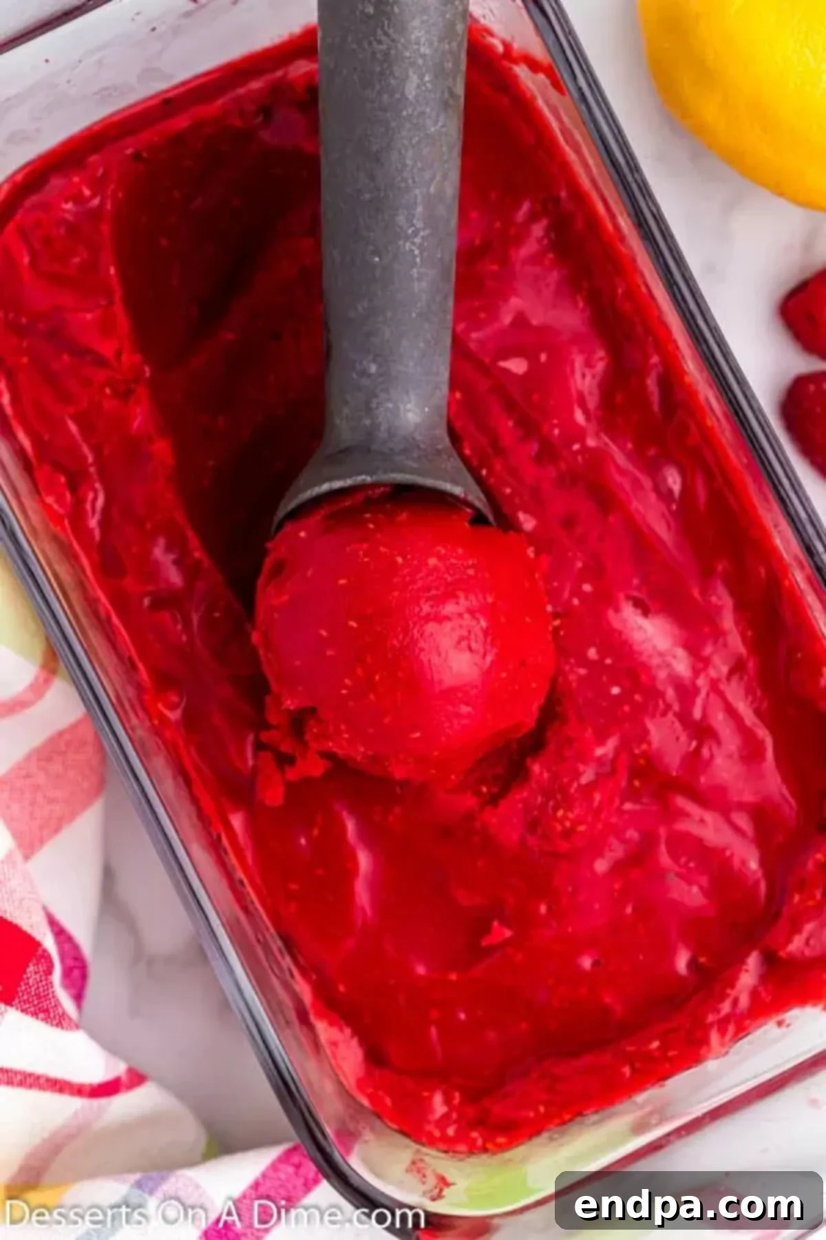 Tangy Raspberry Delight 6 A scoop of vibrant raspberry sorbet in a glass dish, garnished with fresh mint and berries, with an ice cream scoop nearby.