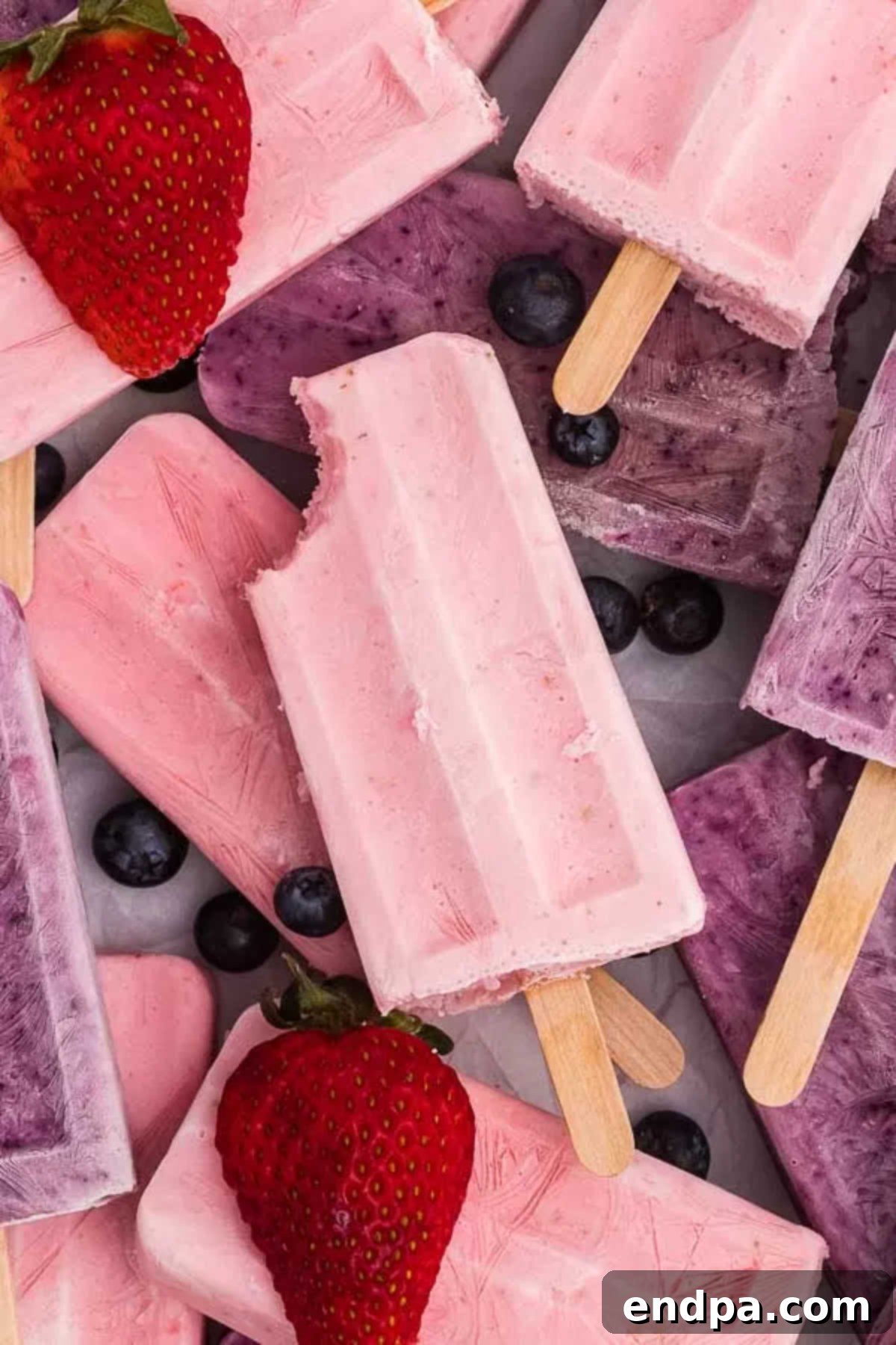 Healthy & Delicious Greek Yogurt Popsicles 2 A stack of vibrant Greek Yogurt Popsicles, beautifully arranged with fresh strawberries and blueberries, showcasing a healthy and refreshing summer treat.