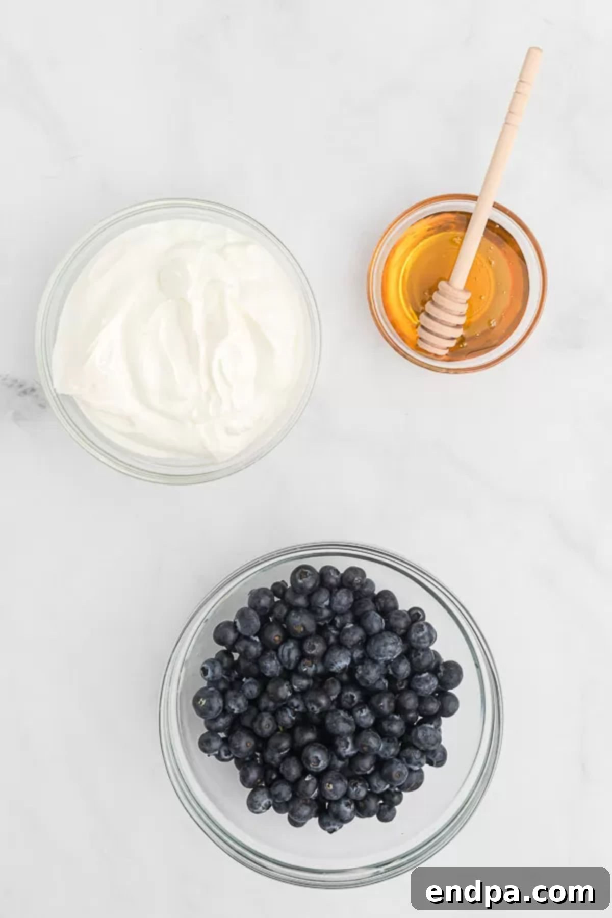 Healthy & Delicious Greek Yogurt Popsicles 3 Three ingredients laid out for Greek Yogurt Popsicles: a bowl of plain Greek yogurt, a mix of fresh berries, and a small jar of honey, emphasizing simplicity and natural goodness.