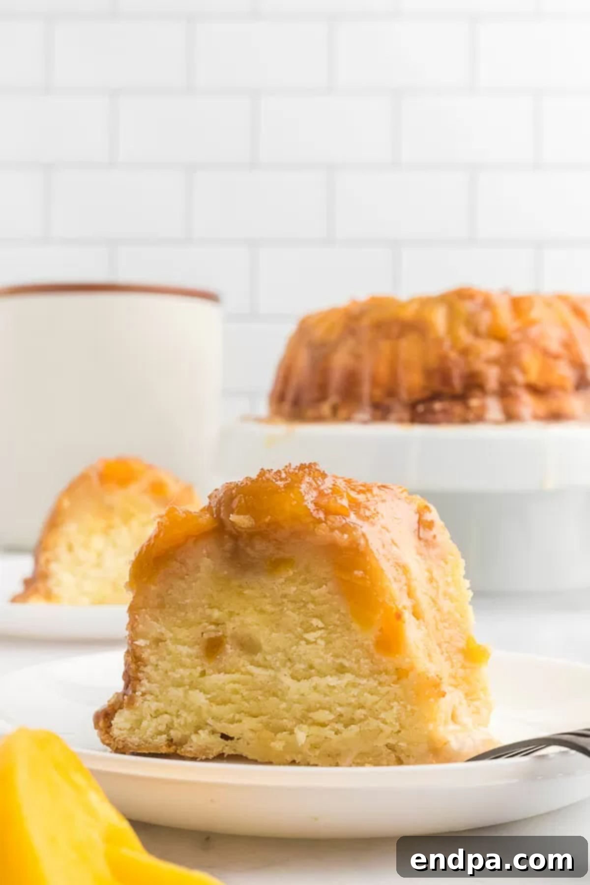 A perfectly sliced piece of Peach Cobbler Pound Cake, showcasing its moist texture and peach filling, resting on a white plate ready to be enjoyed.
