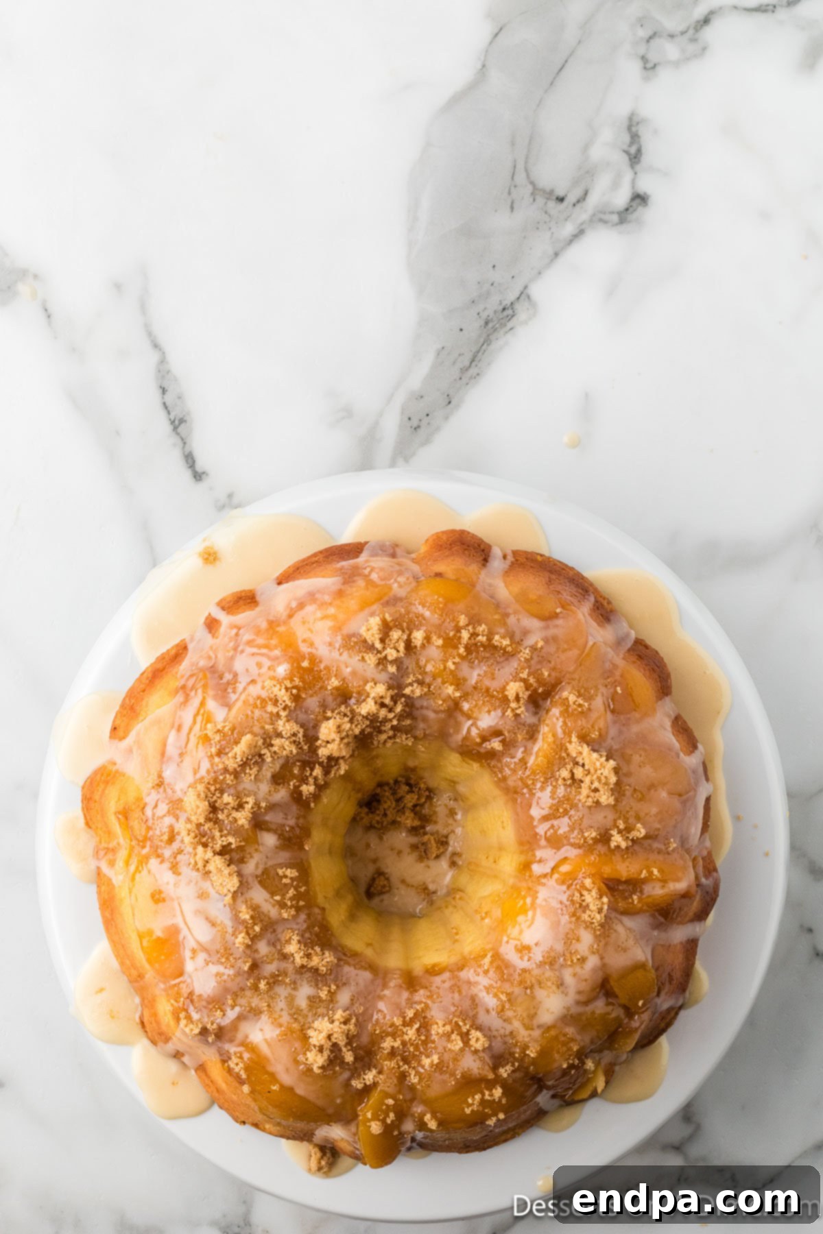 A freshly inverted Peach Cobbler Pound Cake on a serving platter, beautifully drizzled with vanilla glaze.