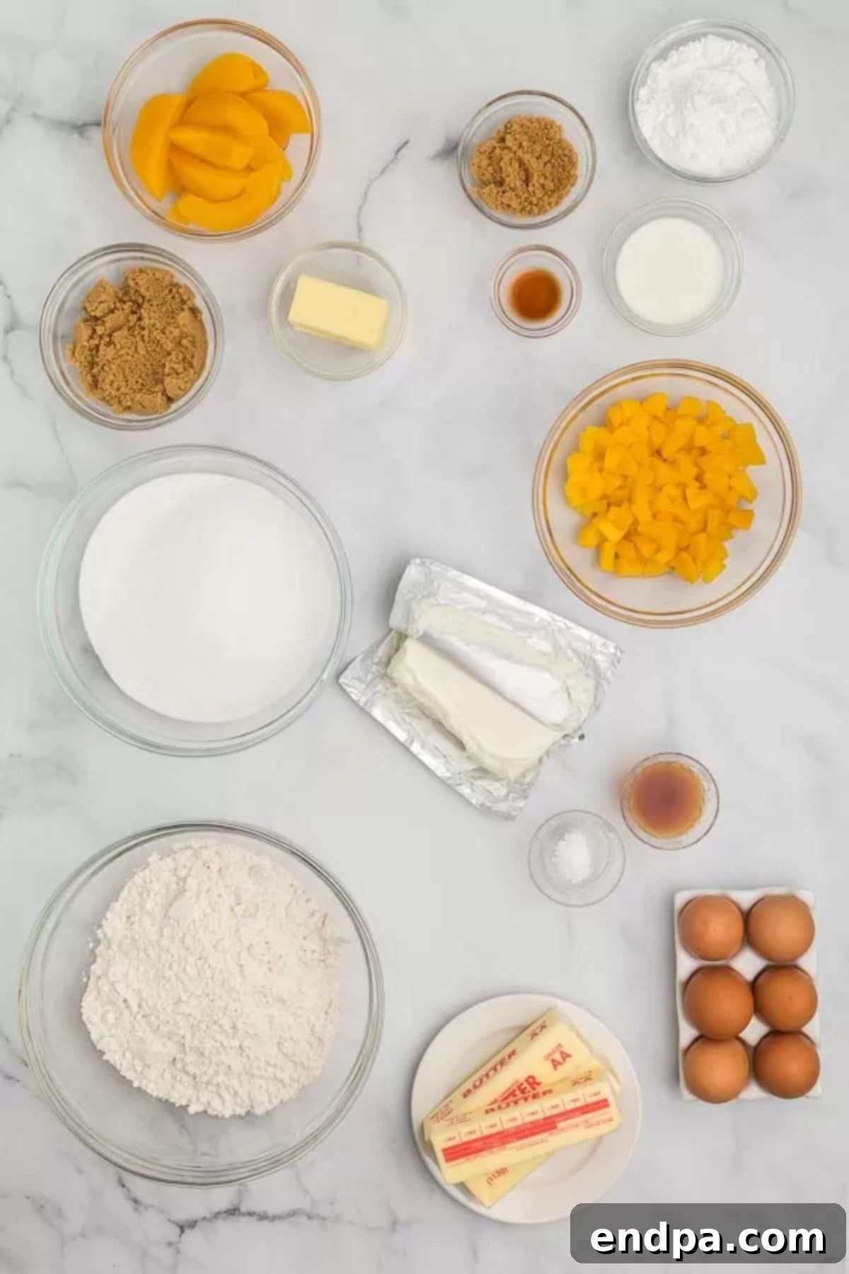 A beautiful display of fresh ingredients for Peach Cobbler Pound Cake, including golden flour, farm-fresh eggs, creamy butter and cream cheese, aromatic vanilla extract, plump diced peaches, rich brown sugar, powdered sugar, and a glass of milk.
