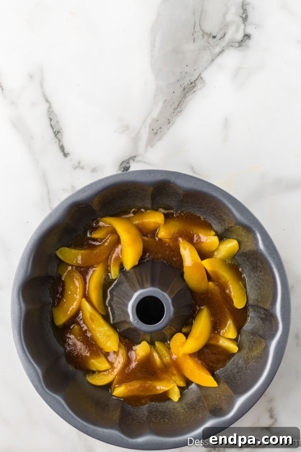 A layer of sliced peaches and brown sugar butter mixture evenly spread at the bottom of a greased bundt pan.