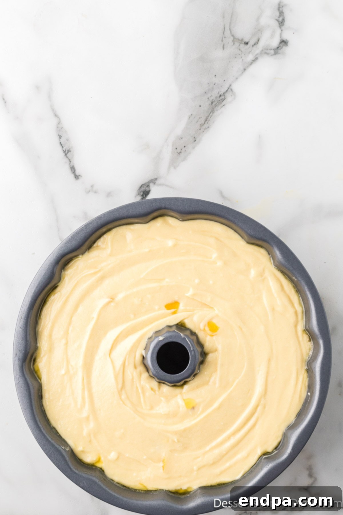 The smooth cake batter being carefully poured over the peach and brown sugar topping in the bundt pan.