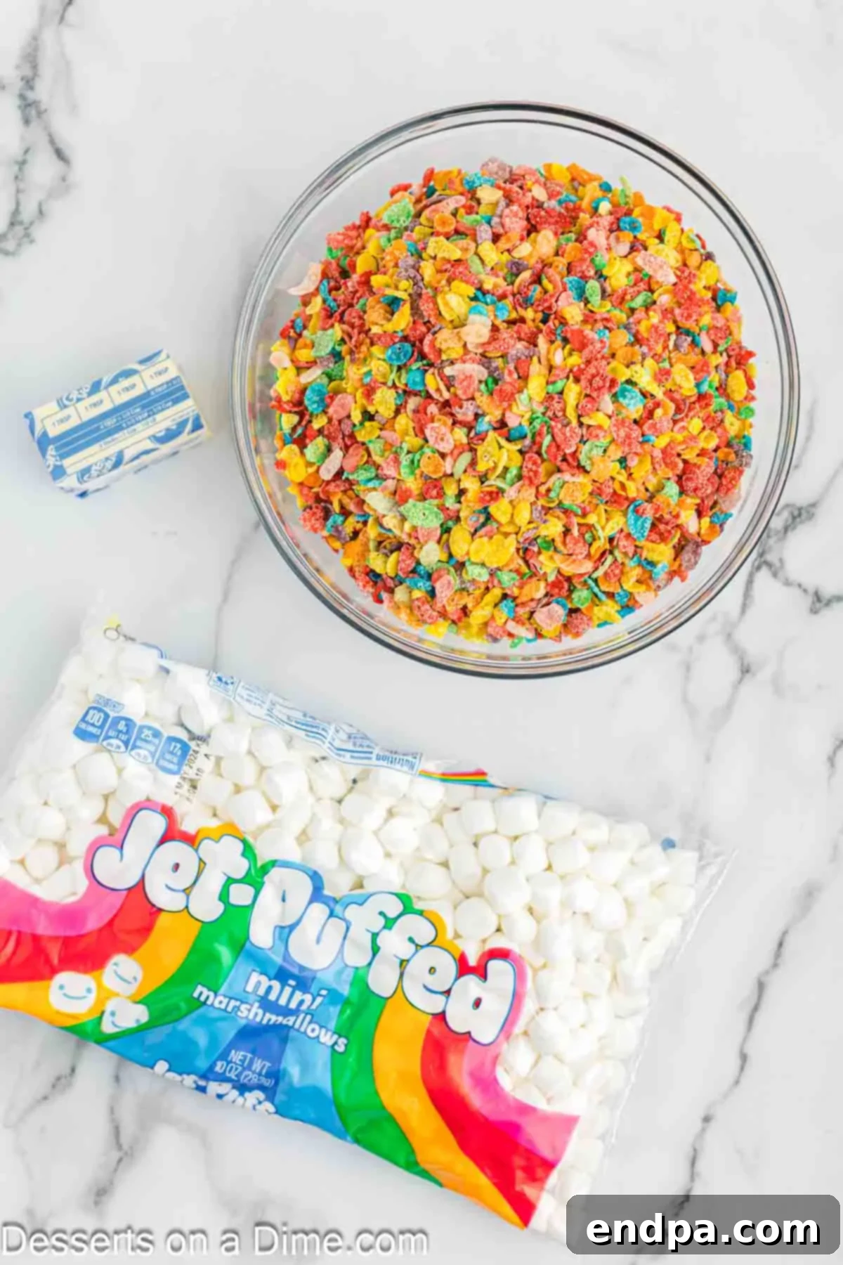 Ingredients for Fruity Pebbles Rice Crispy Treats: a bowl of colorful Fruity Pebbles cereal, a bag of mini marshmallows, and a stick of butter.
