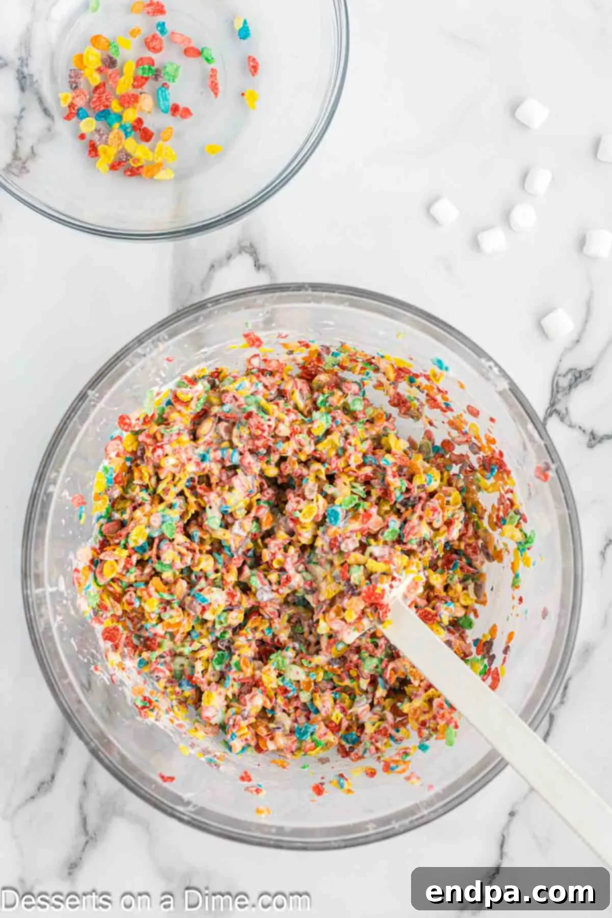 Colorful Fruity Pebbles cereal being added to the melted marshmallow and butter mixture in a large bowl.