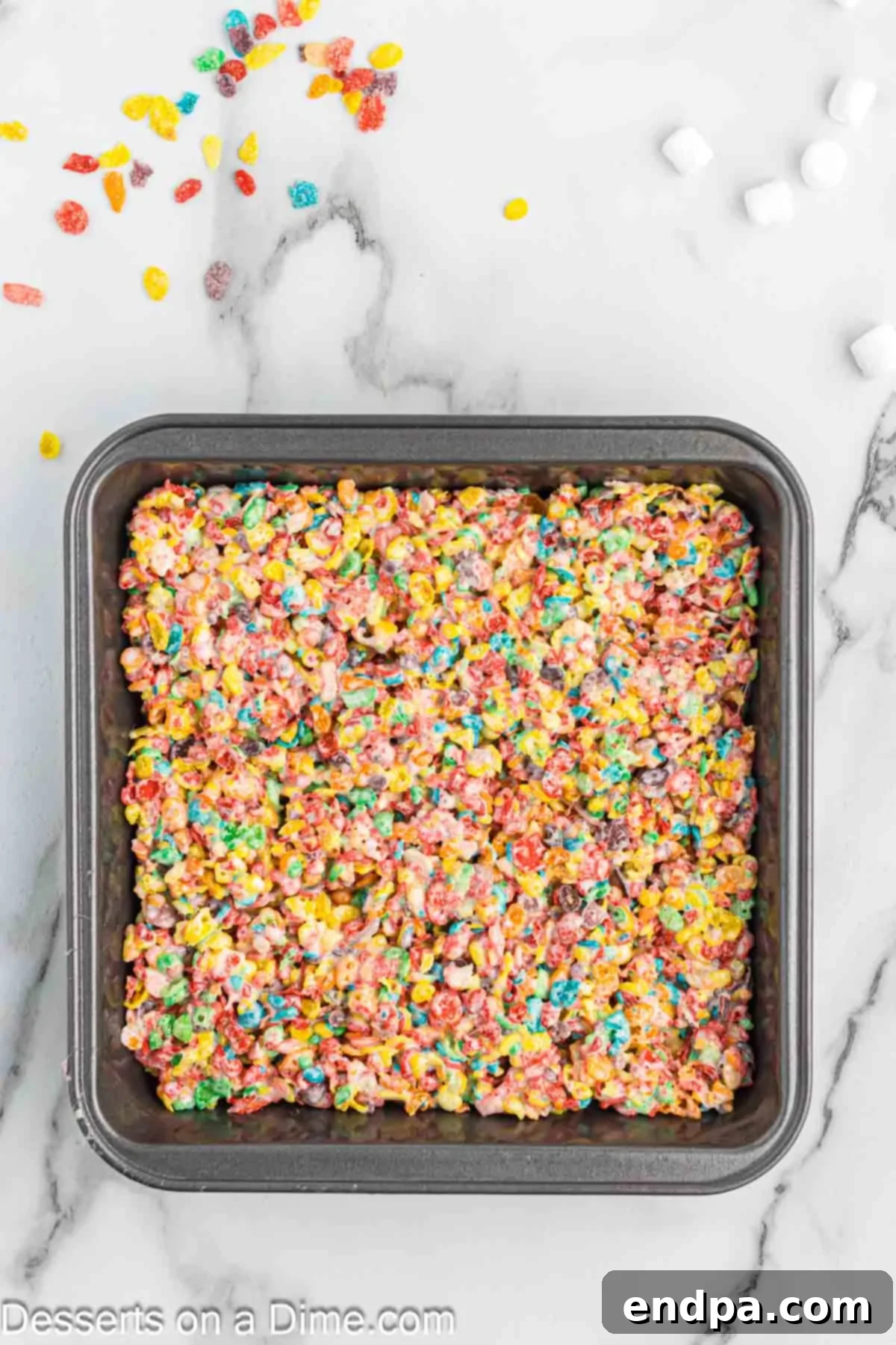The Fruity Pebbles and marshmallow mixture being spread evenly into a prepared baking pan.