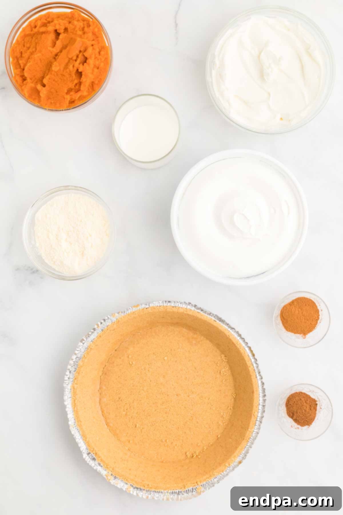 Ingredients for No Bake Pumpkin Pie recipe, including a graham cracker crust, pumpkin puree, cool whip, instant vanilla pudding, milk, and pumpkin pie spices.