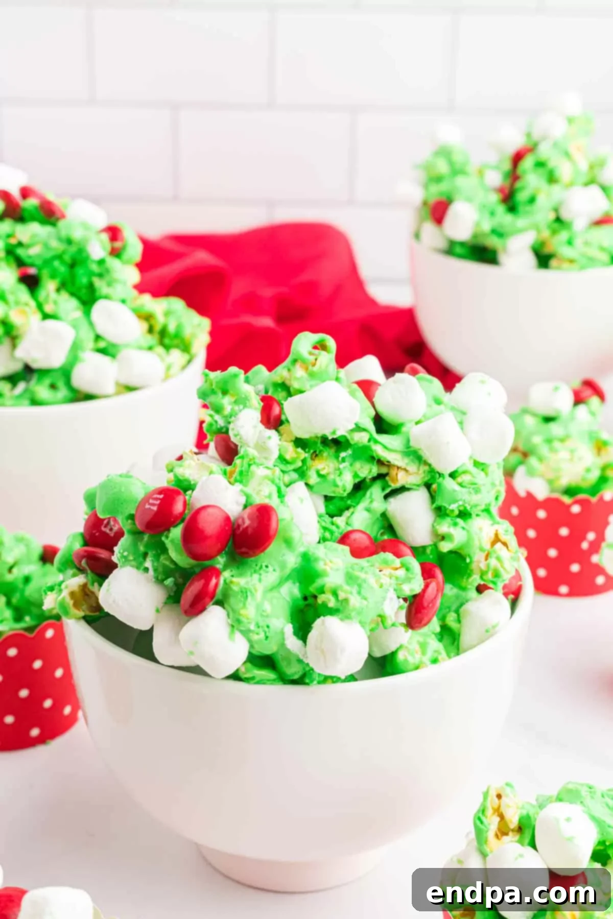 Festive Grinch Popcorn Mix 2 Vibrant green Grinch Popcorn generously topped with red M&Ms and mini marshmallows, served in a festive bowl.