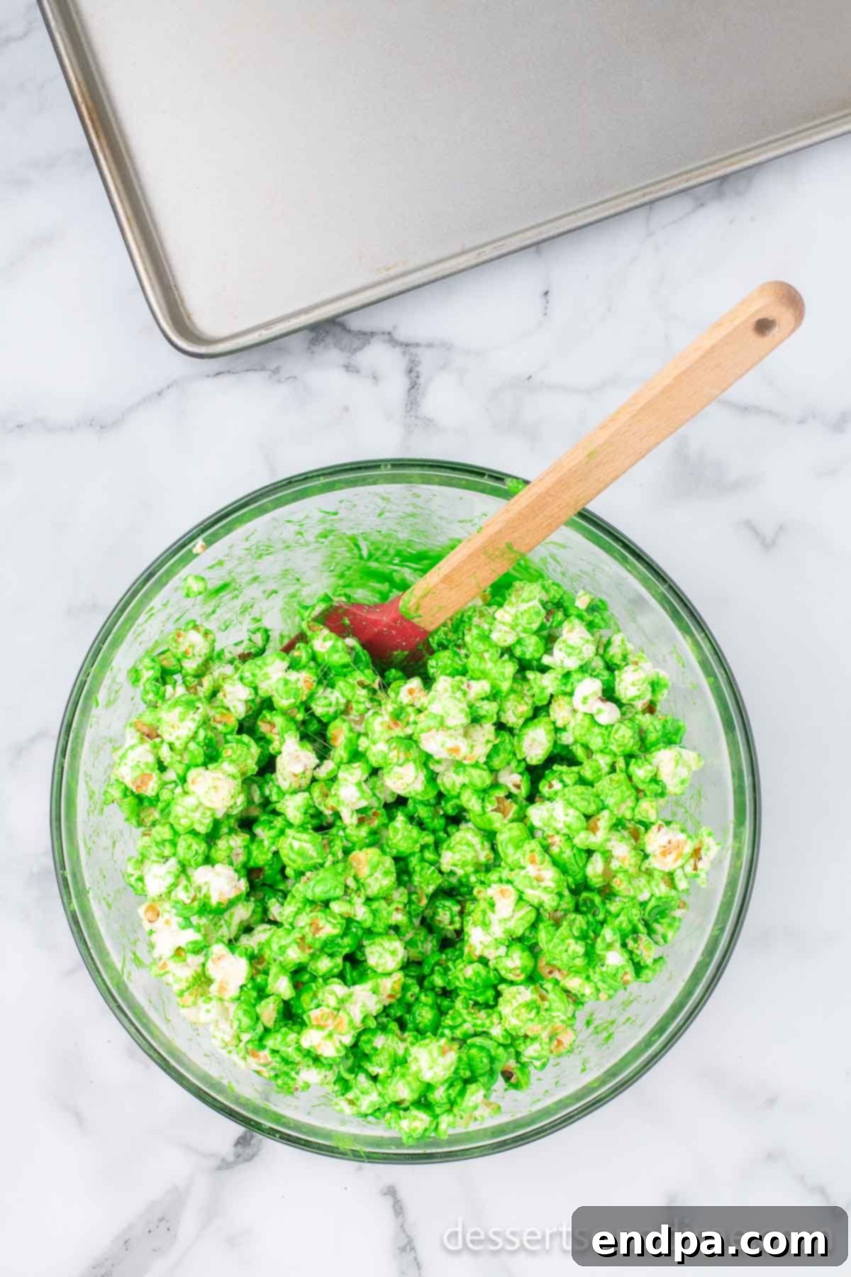 Festive Grinch Popcorn Mix 6 Green marshmallow coating being combined with popcorn in a large bowl, being gently tossed to coat.