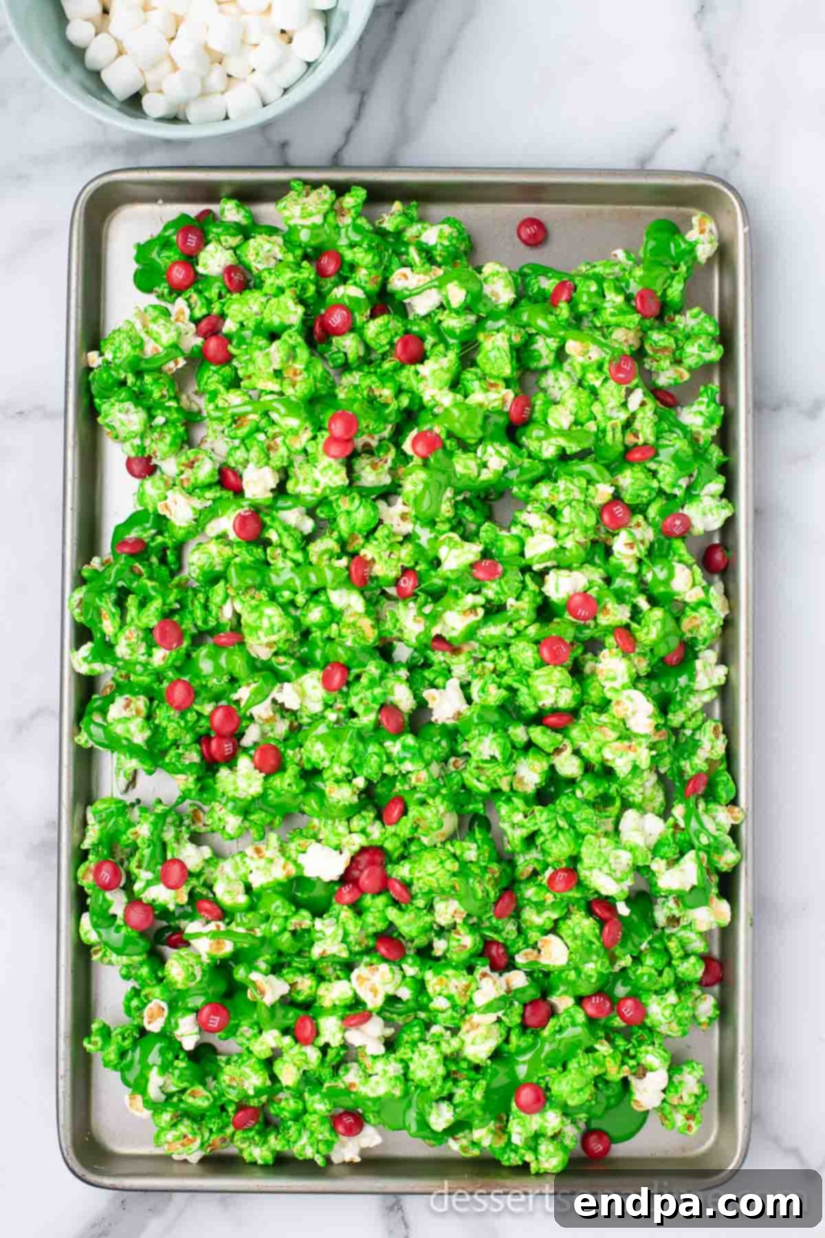 Festive Grinch Popcorn Mix 7 Coated Grinch Popcorn spread out on a baking sheet, with remaining marshmallow mixture drizzled on top.