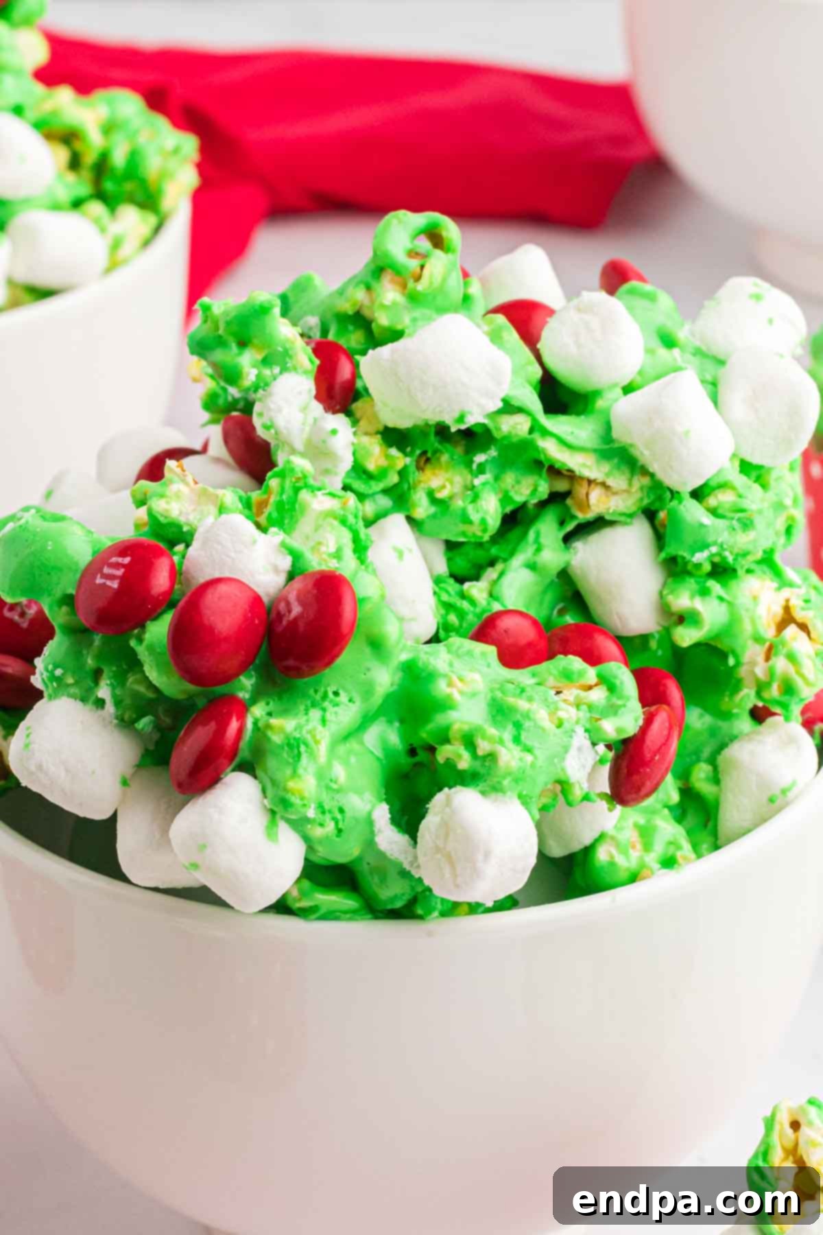 Festive Grinch Popcorn Mix 10 A close-up of a bowl overflowing with brightly colored Grinch Popcorn, showing the vibrant green, red M&Ms, and fluffy marshmallows.