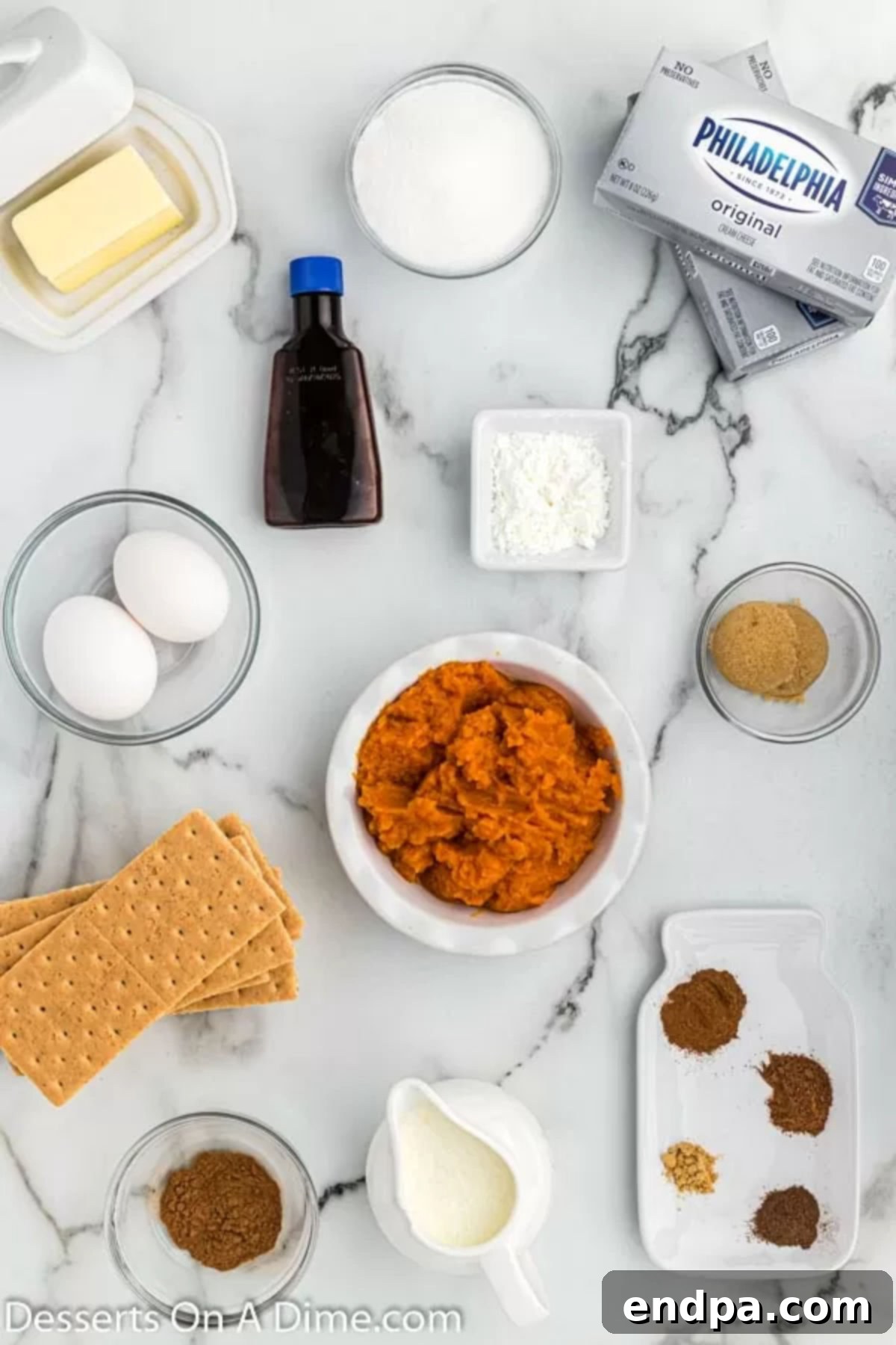 A flat lay of ingredients for Instant Pot Pumpkin Cheesecake, including graham cracker sheets, brown sugar, softened cream cheese, pumpkin puree, vanilla extract, eggs, heavy cream, and various pumpkin spices.