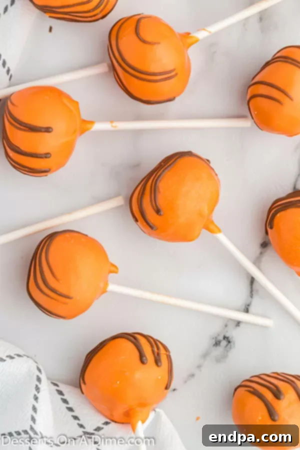 Finished pumpkin cake pops, set and ready to be enjoyed, with a beautiful orange coating and chocolate drizzle.