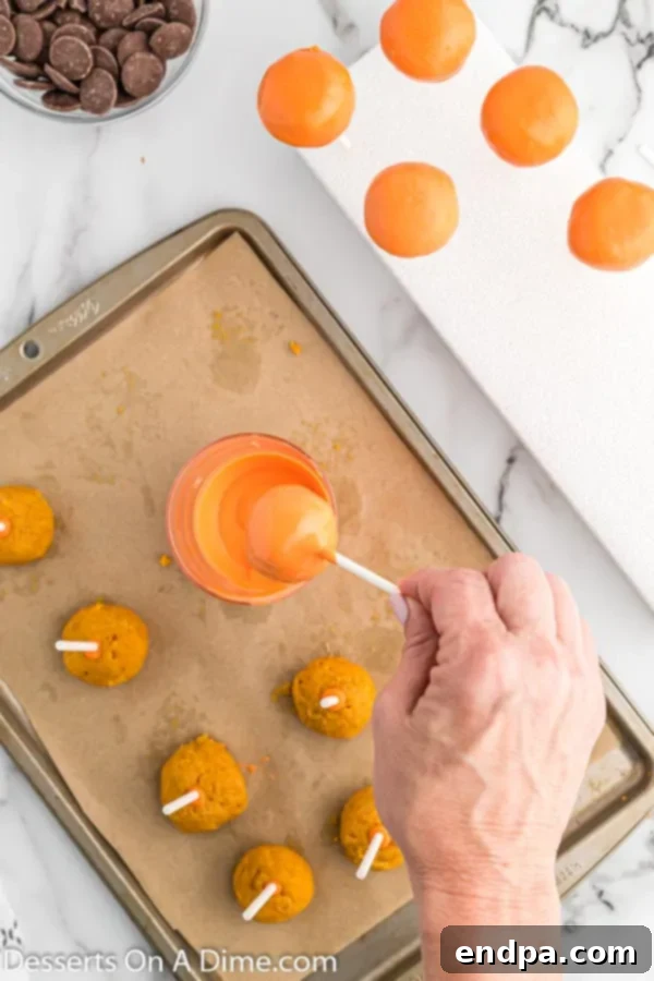 Pumpkin cake pops being dipped into melted orange candy melts.