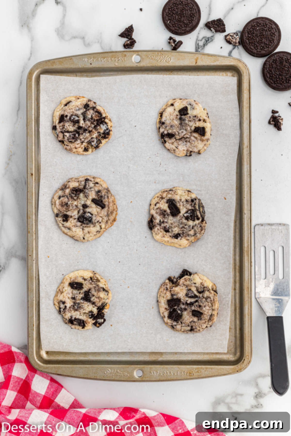 Freshly baked Oreo cheesecake cookies cooling on a baking sheet.