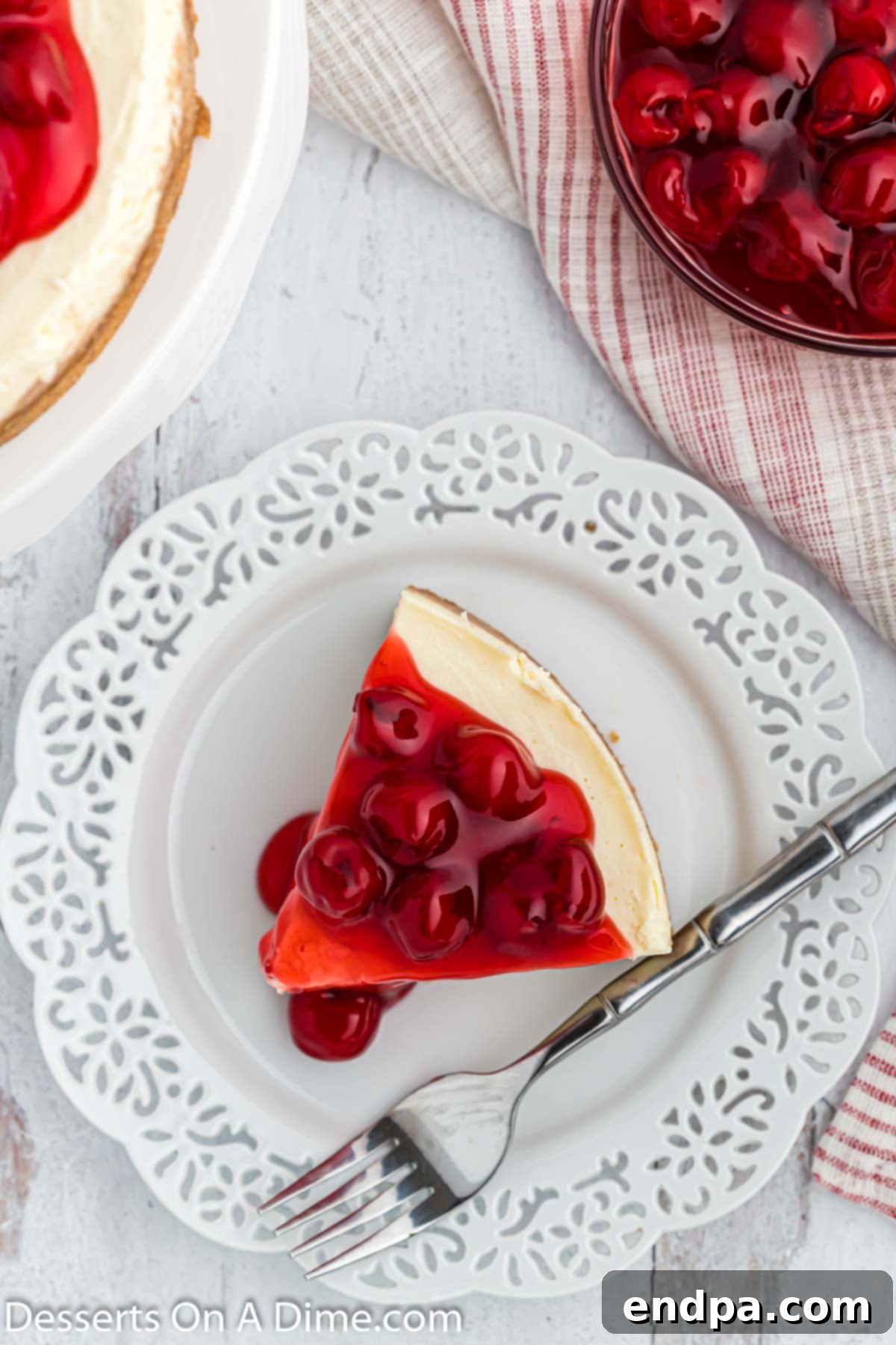 A delectable slice of Instant Pot cheesecake, garnished with fresh cherry pie filling and a light dusting of powdered sugar.