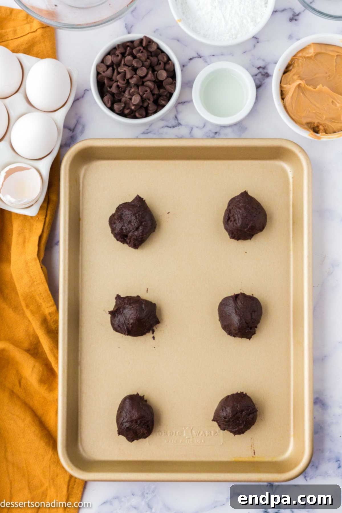 Ultimate Buckeye Brownie Delights 5 Round brownie batter balls arranged on a baking sheet, each with a thumbprint indentation in the center.
