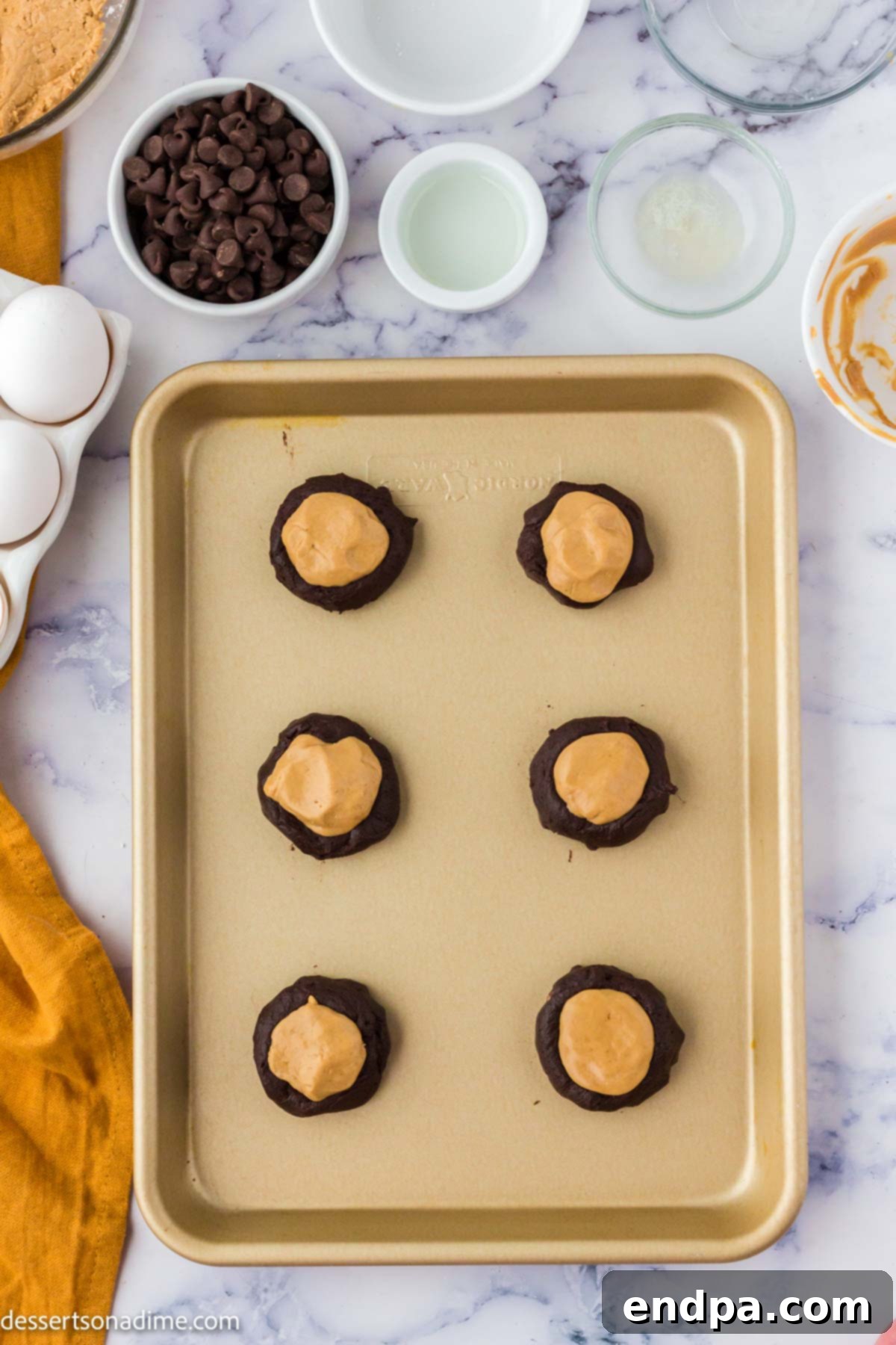 Ultimate Buckeye Brownie Delights 8 A baking sheet with unbaked brownie cookies, each with a peanut butter ball gently pressed into its indentation.
