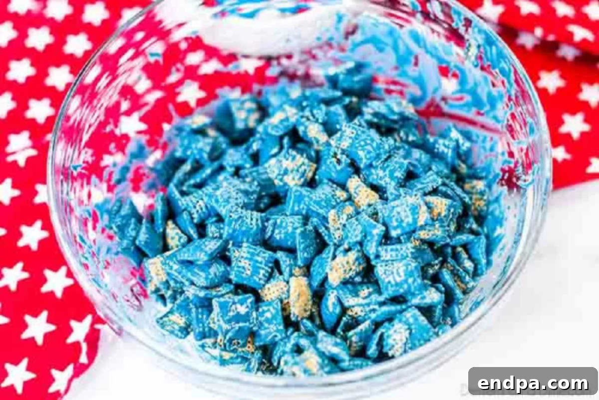 Patriotic Puppy Chow 5 Chex cereal being coated with the melted blue candy mixture in a large bowl.
