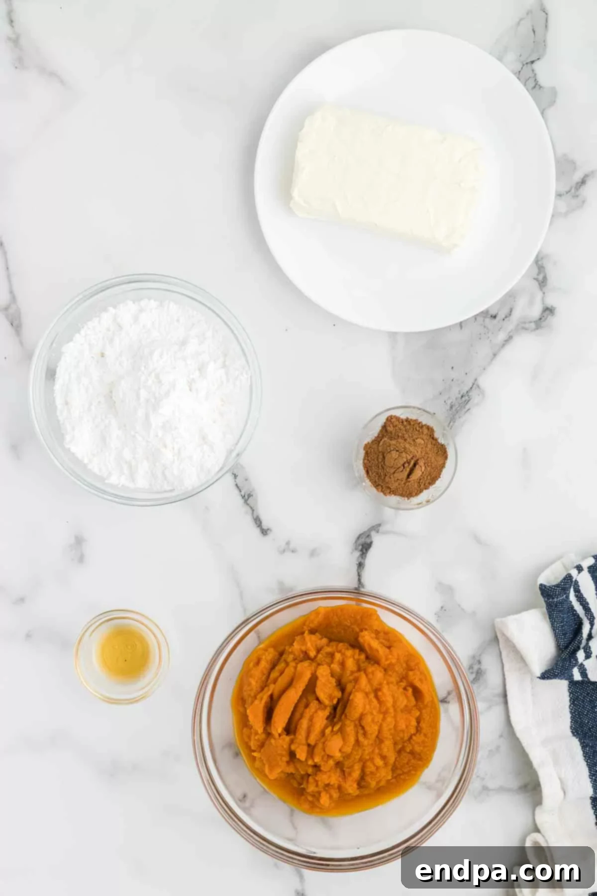 All essential ingredients for creamy pumpkin dip, including a can of pumpkin puree, a block of cream cheese, powdered sugar, pumpkin pie spice, and vanilla extract, arranged neatly on a wooden surface.
