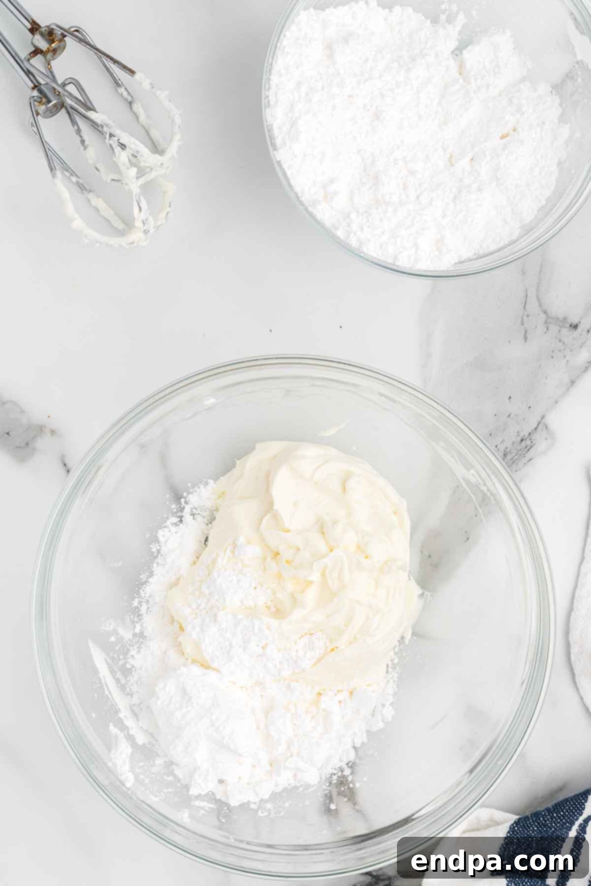 Sifted powdered sugar being added to the fluffy cream cheese in a mixing bowl.
