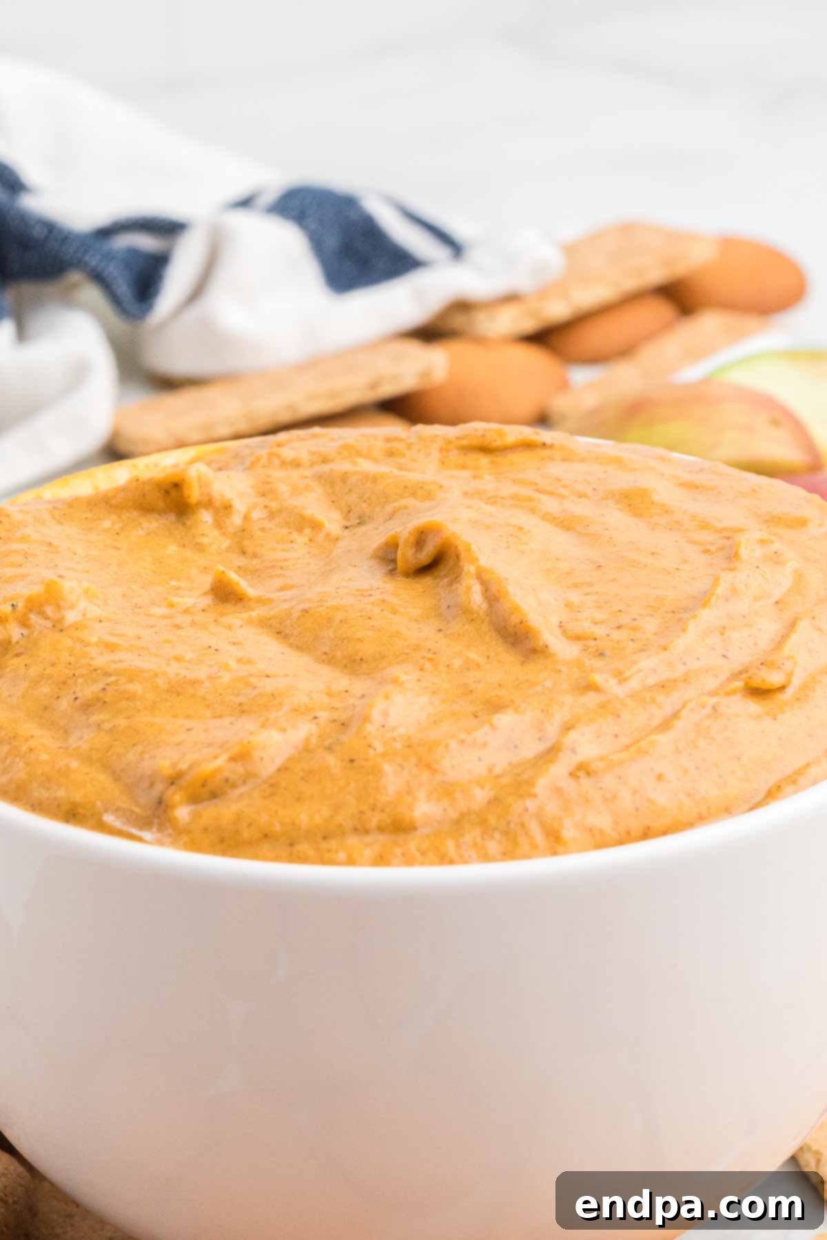 The fully mixed pumpkin dip, creamy and orange, being spooned into an elegant white serving dish for chilling.