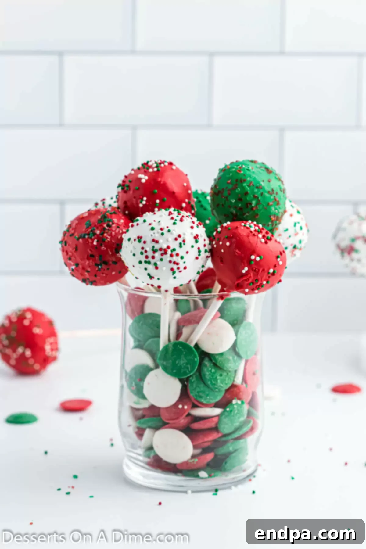 Festive Christmas cake pops arranged in a vase with candy melts and sprinkles.