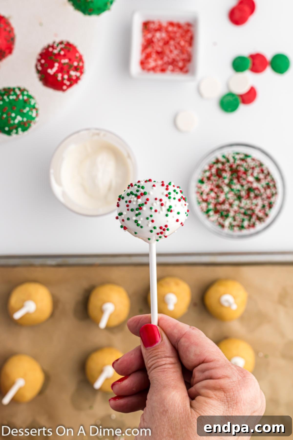 A Christmas cake pop topped with colorful sprinkles, held by a lollipop stick.
