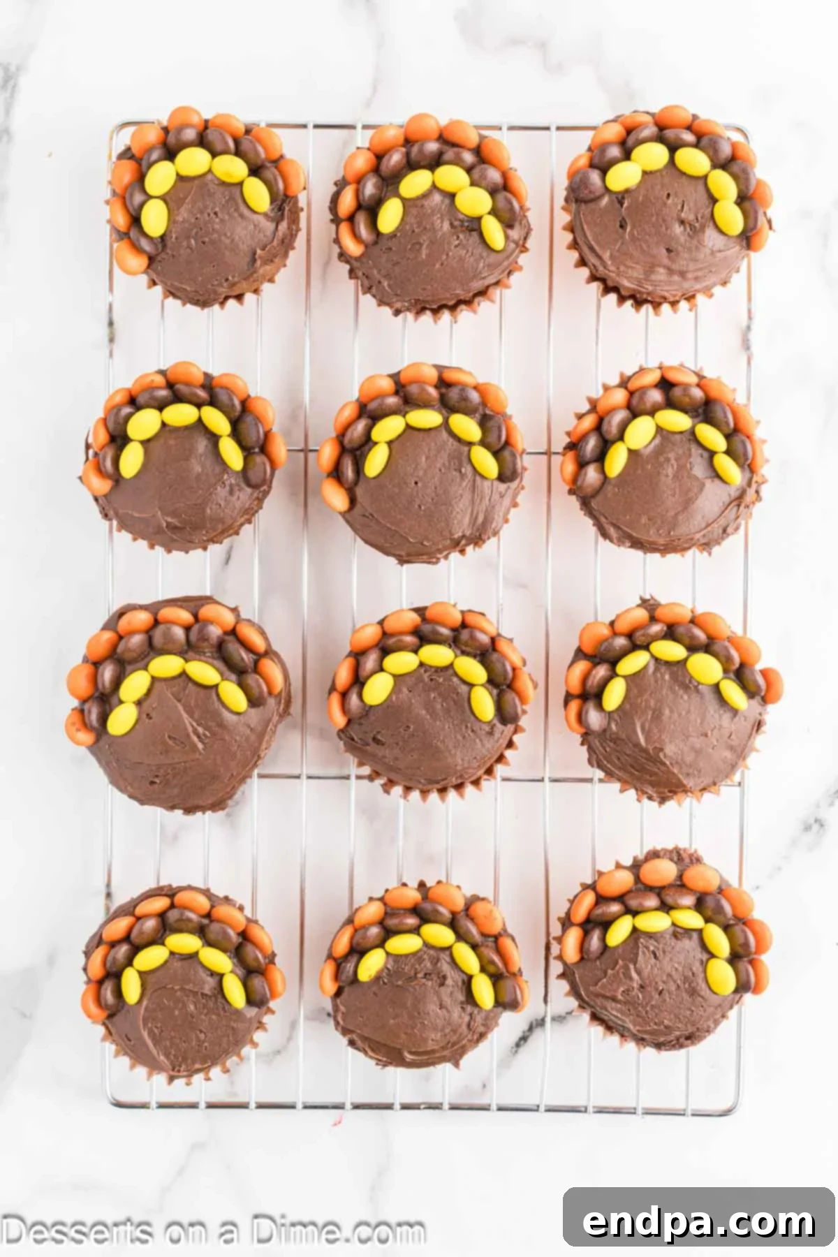 A cupcake adorned with three distinct rows of colorful Reese's Pieces, artfully arranged to resemble turkey feathers.