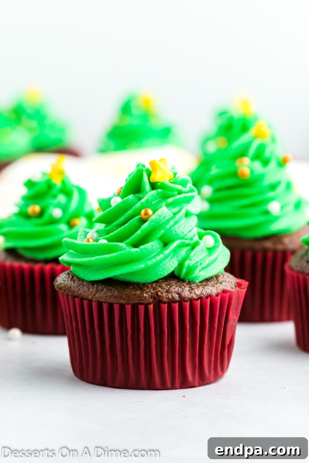 Close up photo of Christmas tree cupcakes, beautifully decorated with green frosting, candy balls as ornaments, and yellow sugar stars on top.