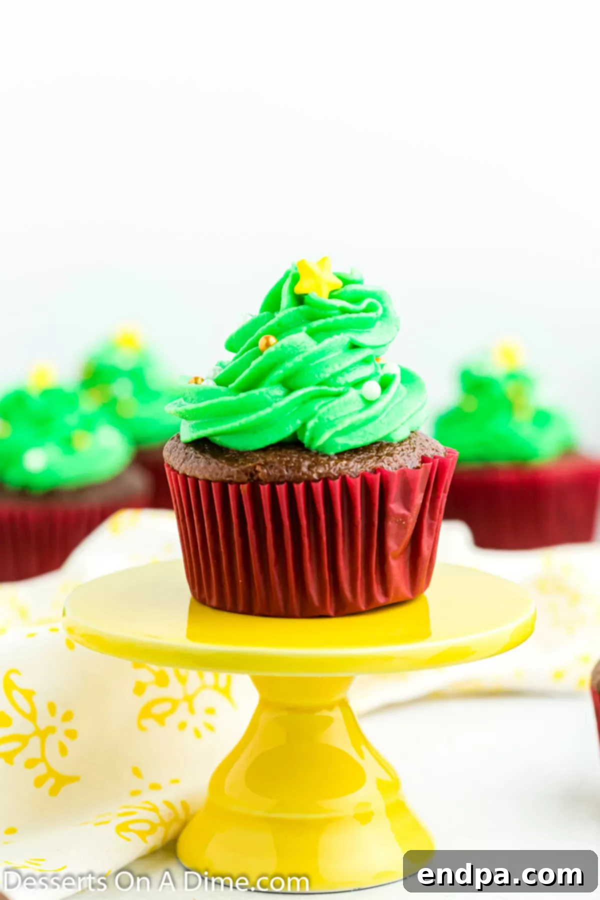 Close up photo of Christmas tree cupcakes with green piped frosting, adorned with colorful candy ornaments and yellow sugar stars on top, ready to be enjoyed.