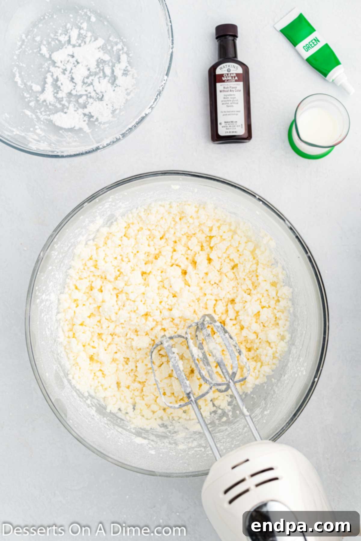 Powdered sugar being gradually added to the mixing bowl with creamed shortening and butter, and then mixed until fully incorporated.