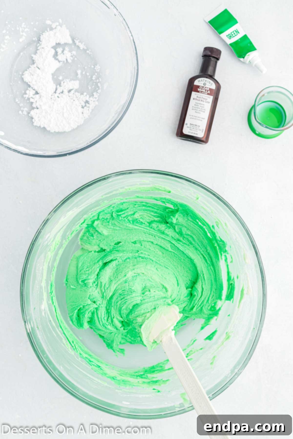 Green gel food coloring being mixed into the white frosting, transforming it into a vibrant Christmas tree green.