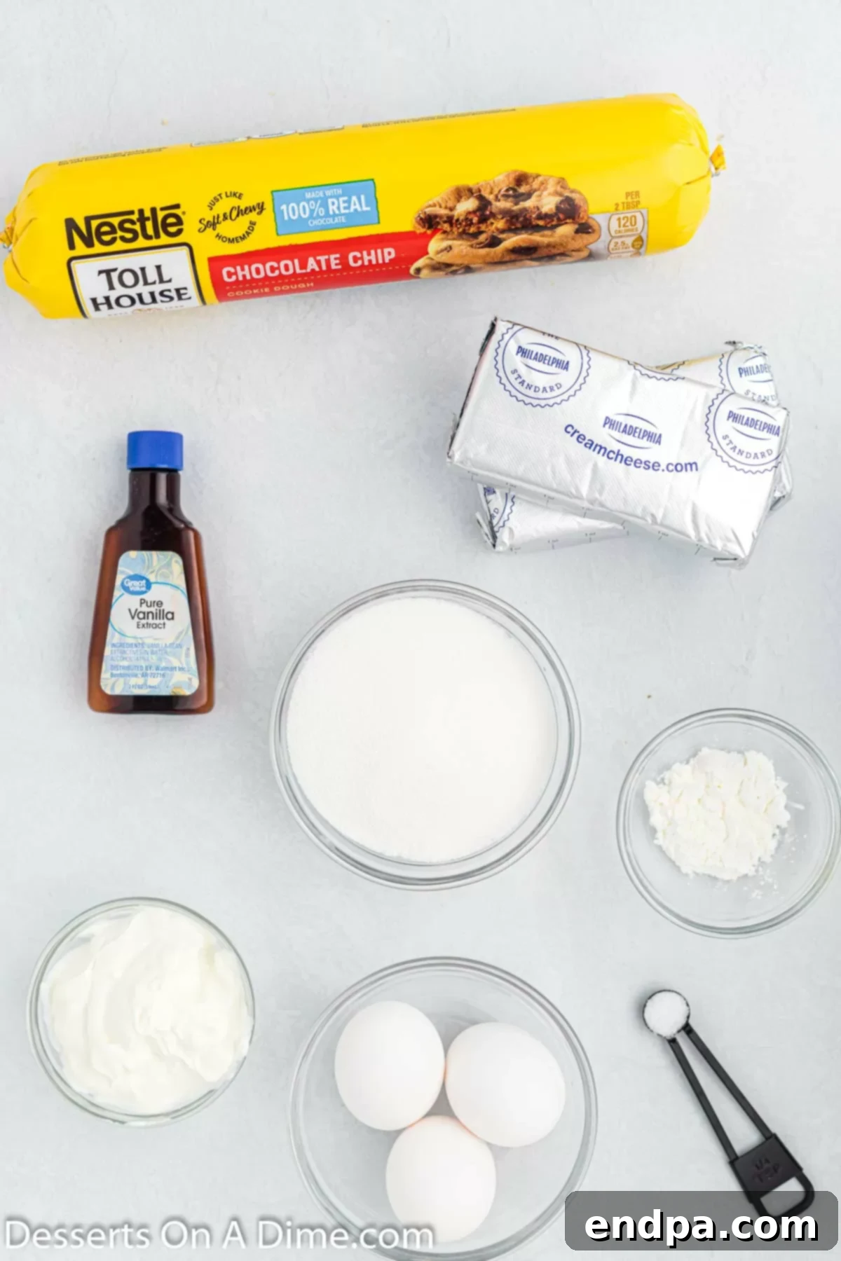 Cookie Dough Dream Cheesecake 3 A visual display of all the key ingredients needed for Chocolate Chip Cookie Cheesecake, including packaged cookie dough, blocks of cream cheese, vanilla extract, and eggs.