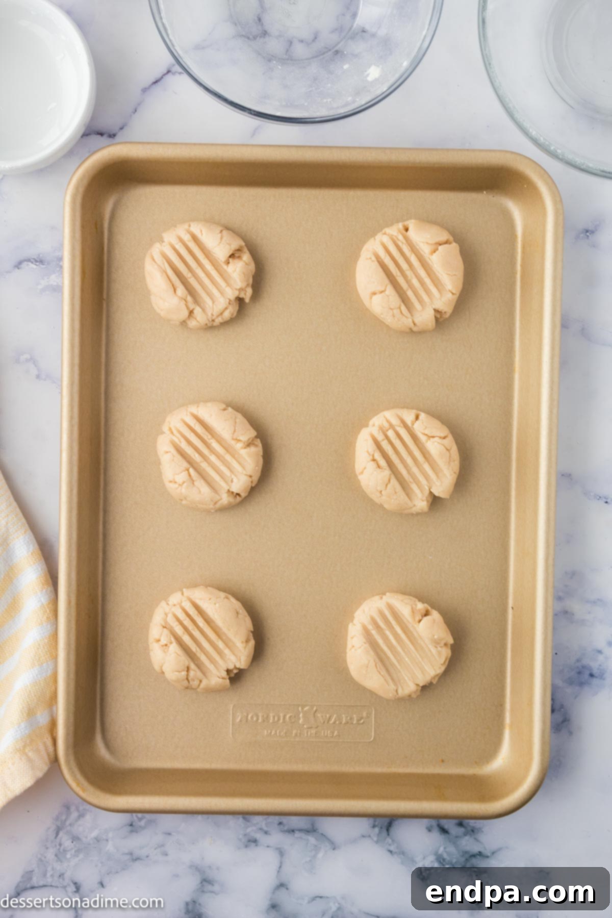 Cookie dough shaped into flat cookies and arranged on a baking sheet before baking.
