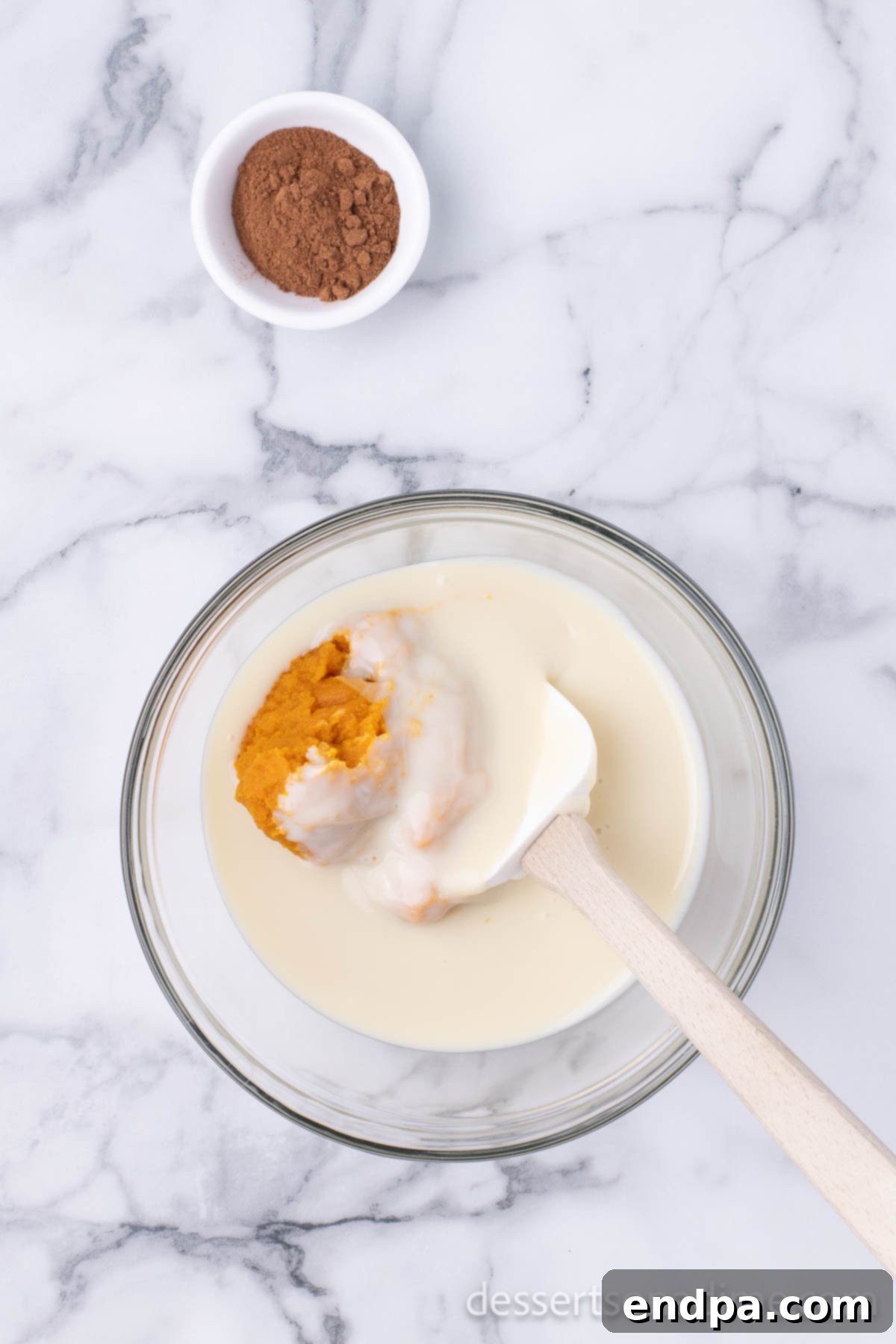 Sweetened condensed milk being poured into the mixing bowl with pumpkin puree, preparing for combination.
