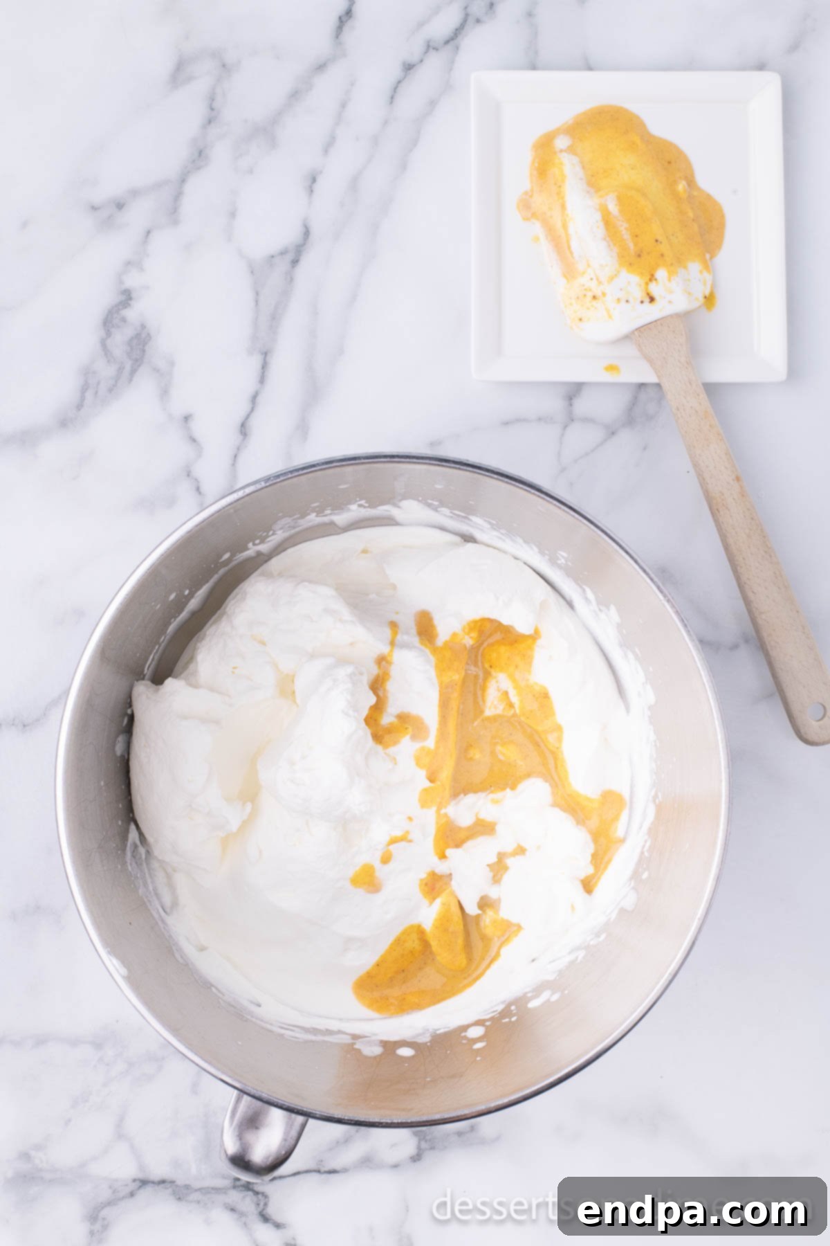 The spiced pumpkin and sweetened condensed milk mixture being gently folded into the bowl of whipped heavy cream.