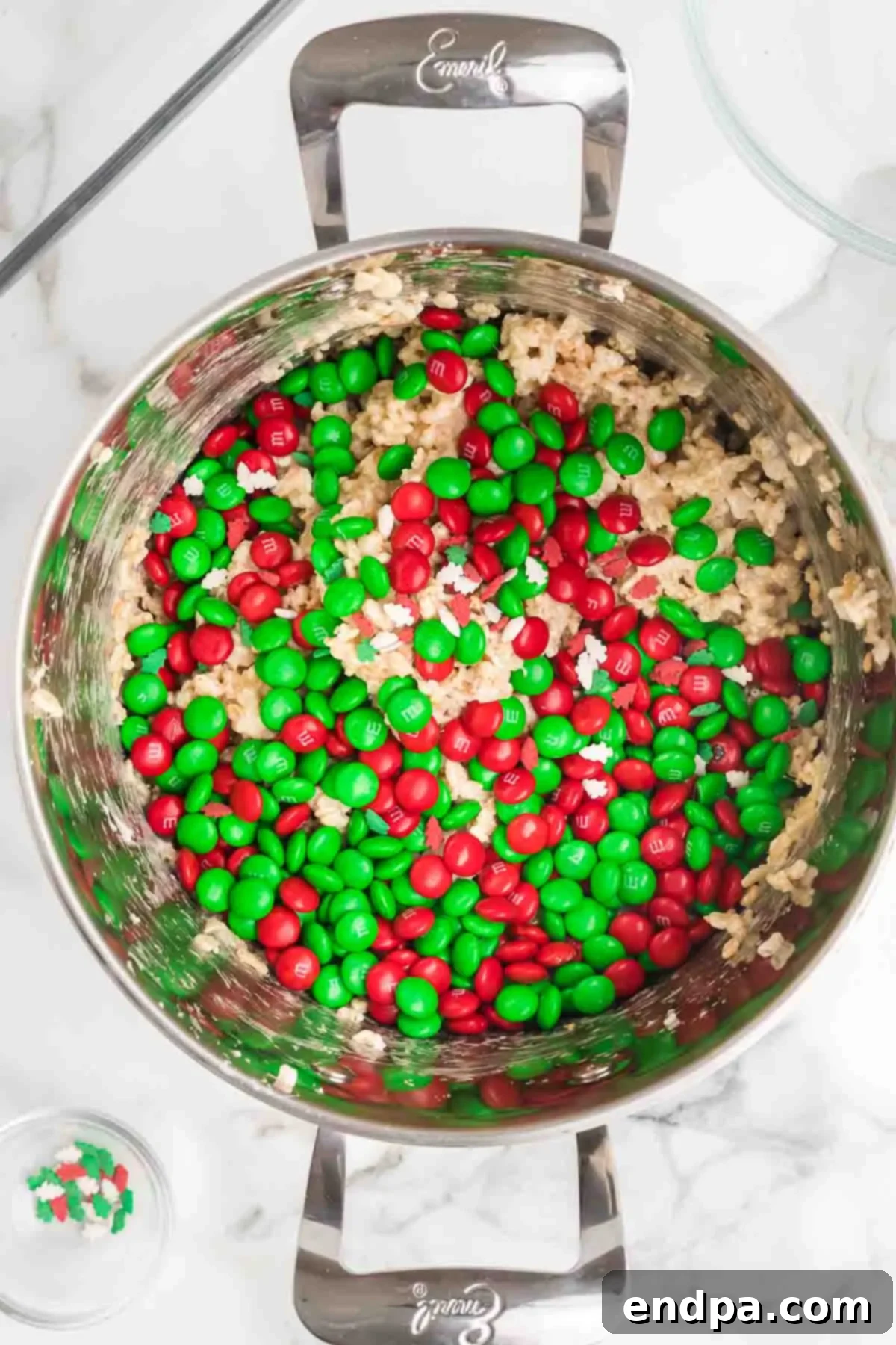 Jolly Krispie Delights 8 Red and green M&M's and festive sprinkles being gently folded into the cereal mixture in a saucepan.