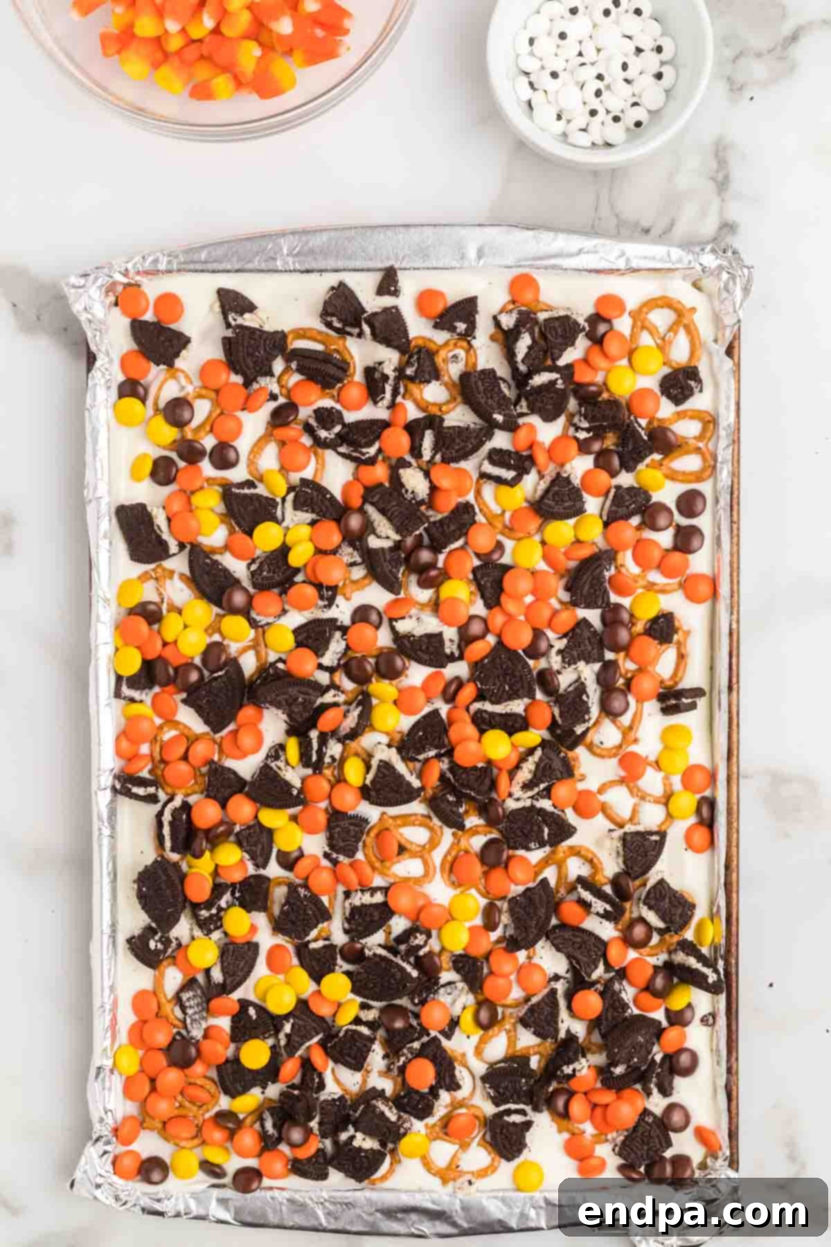 Halloween bark in a sheet pan, generously topped with various candies, cookies, and sprinkles.