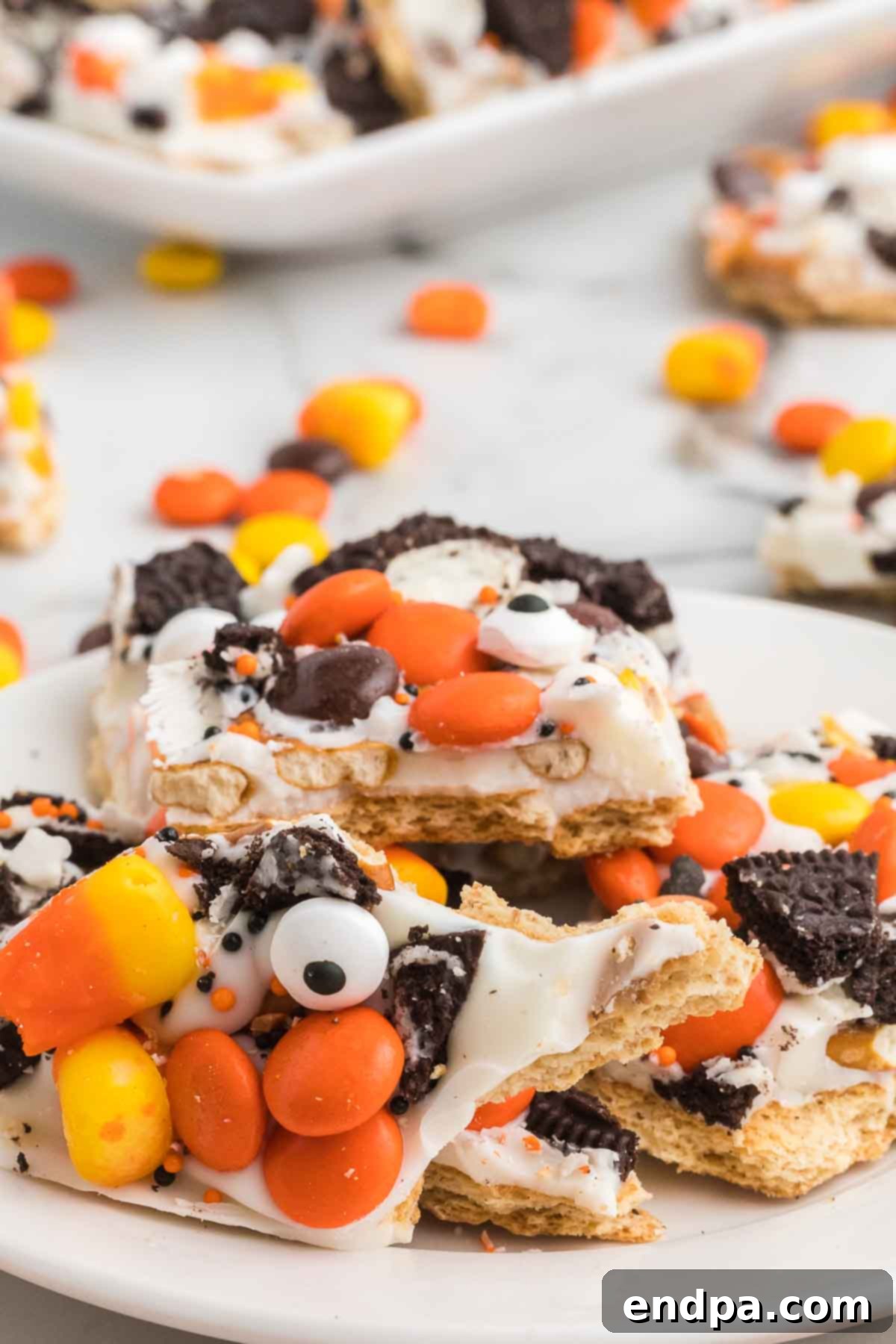 Close up photo of Halloween Candy Bark on a platter broken into pieces, revealing the layers of chocolate, pretzels, Oreos, and various candies.