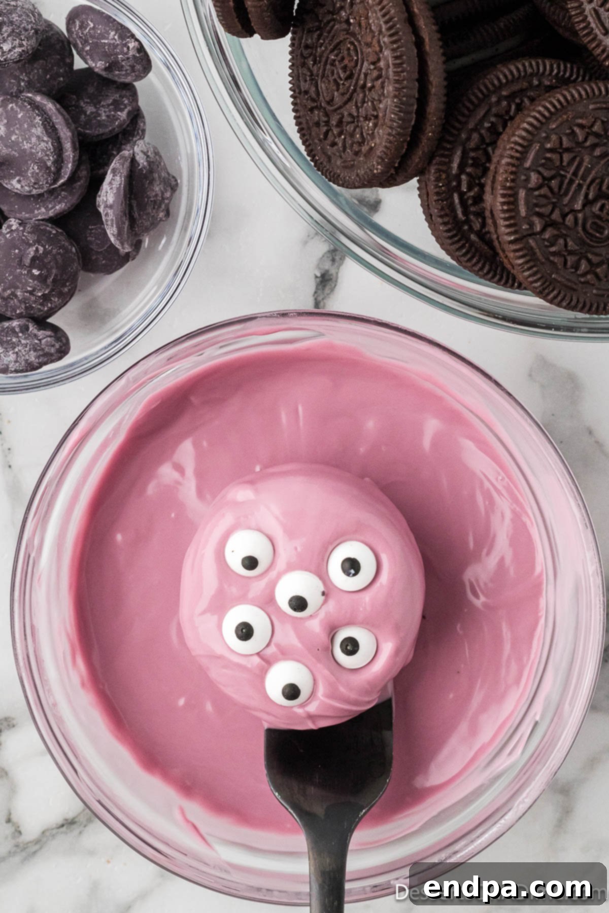Candy eyes being carefully placed onto a freshly coated Oreo cookie before the candy sets.