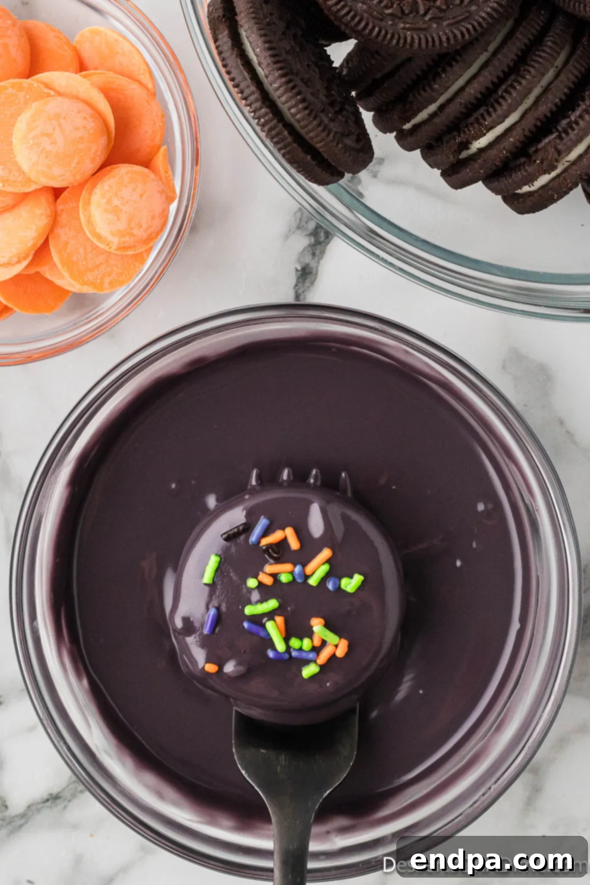 Halloween sprinkles being added to a freshly coated Oreo cookie, still wet with candy melts.