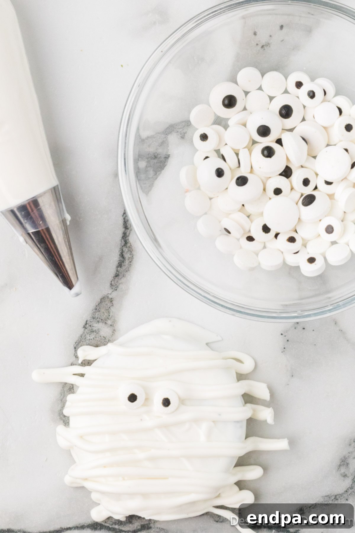 Melted white chocolate drizzled artfully over an Oreo cookie with candy eyes, creating a mummy effect.
