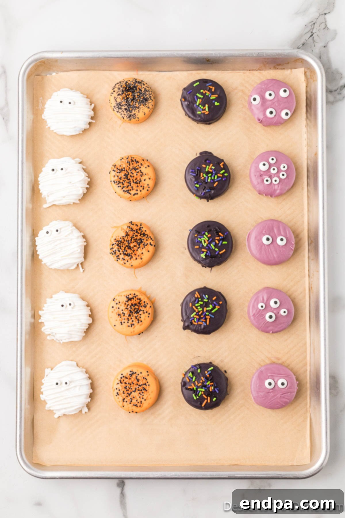 An assortment of freshly decorated Halloween chocolate covered Oreos arranged on a baking sheet, allowing them to set.
