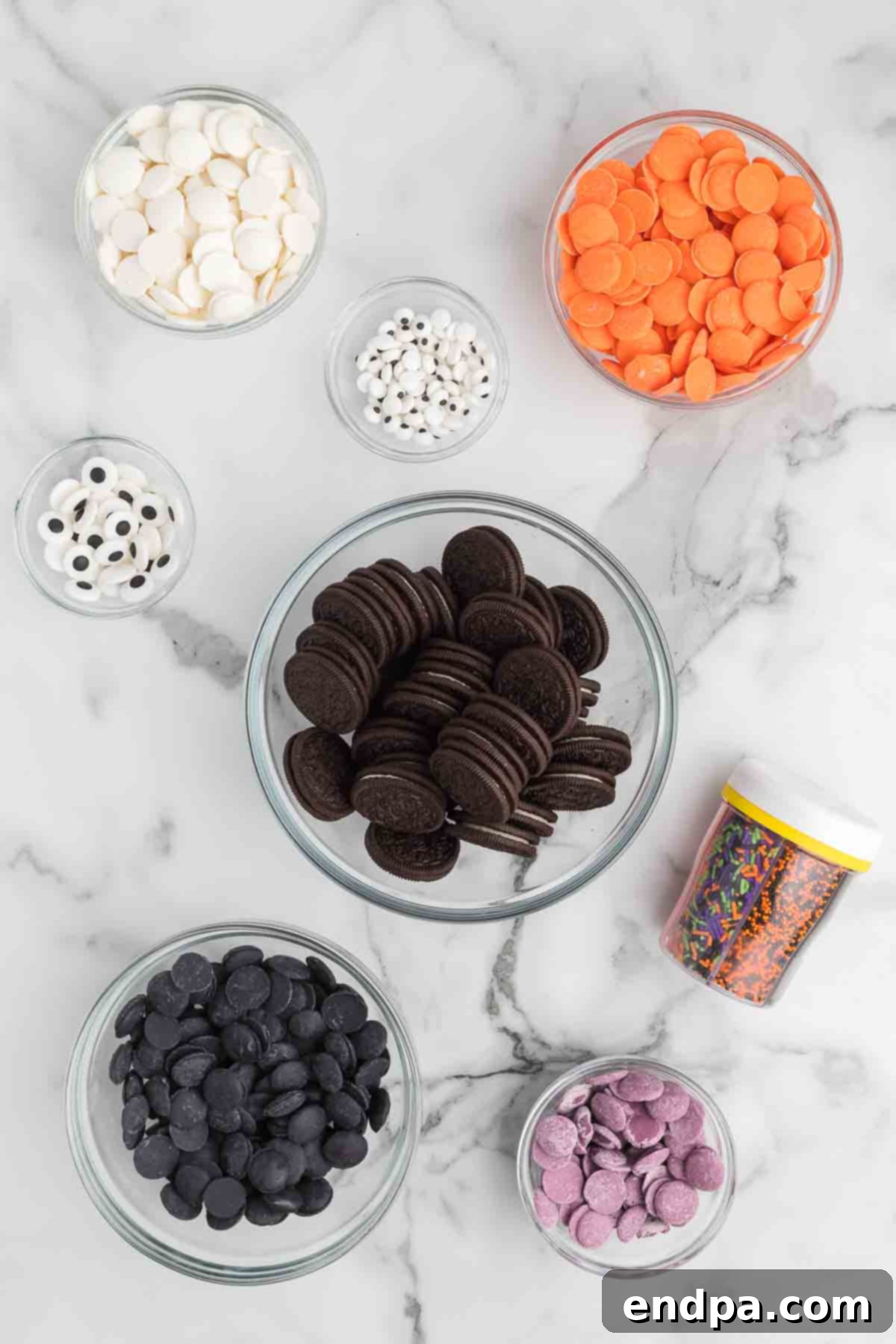 Ingredients for Halloween chocolate covered oreos: Oreo cookies, various colors of candy melts, Halloween sprinkles, and candy eyes laid out on a surface.