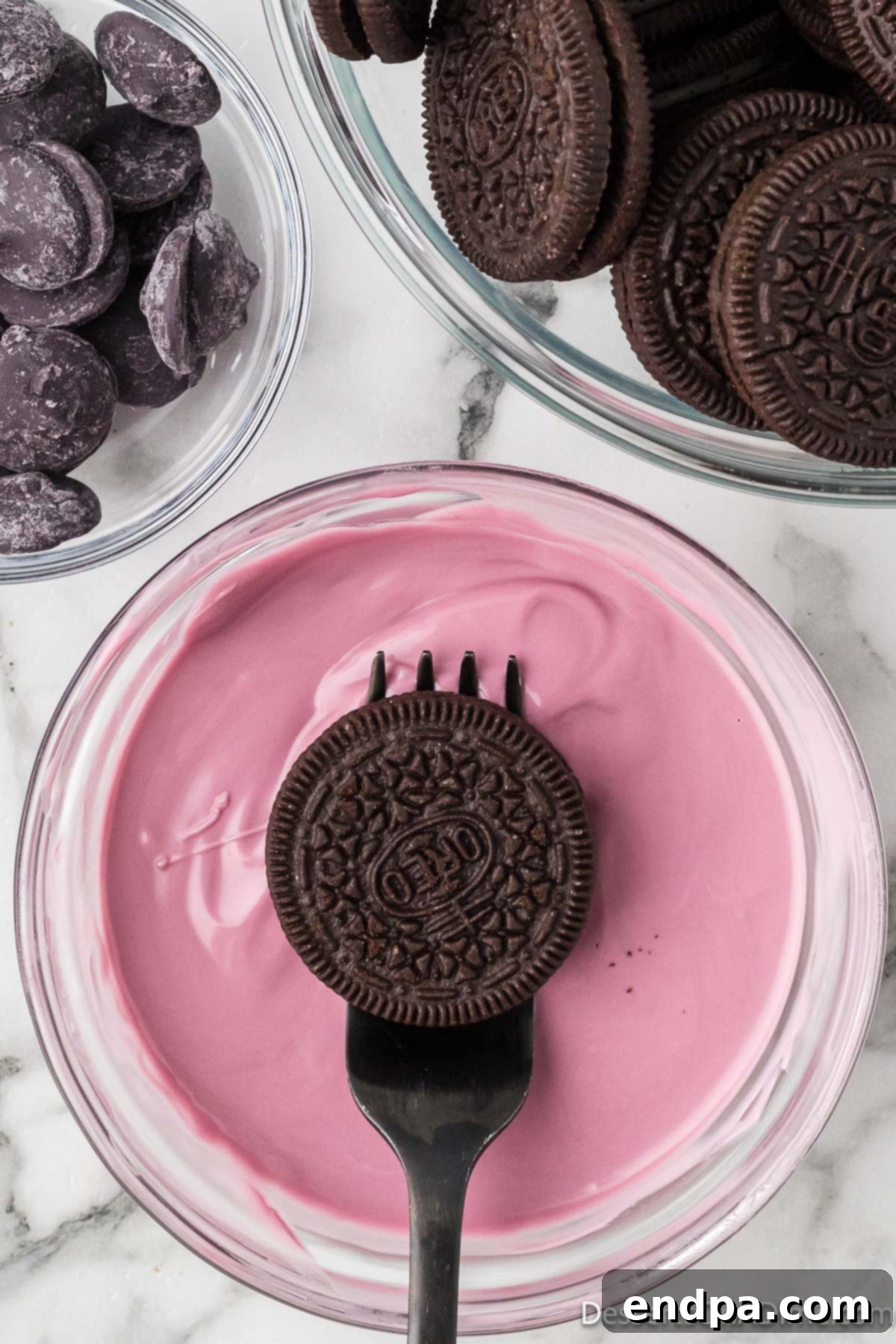 An Oreo cookie being carefully dipped into a bowl of melted purple candy.