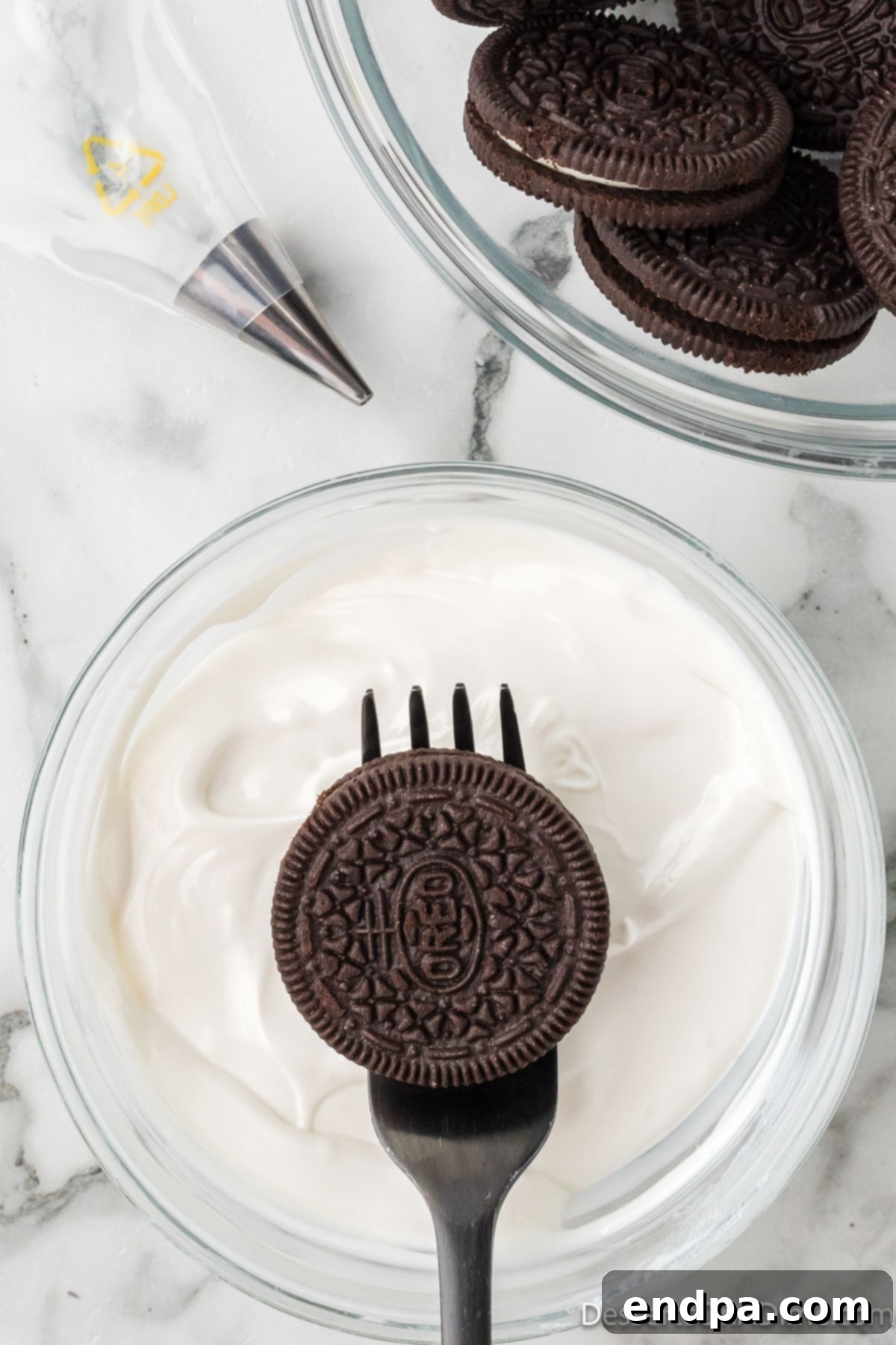 An Oreo cookie being dipped into a bowl of melted white candy.