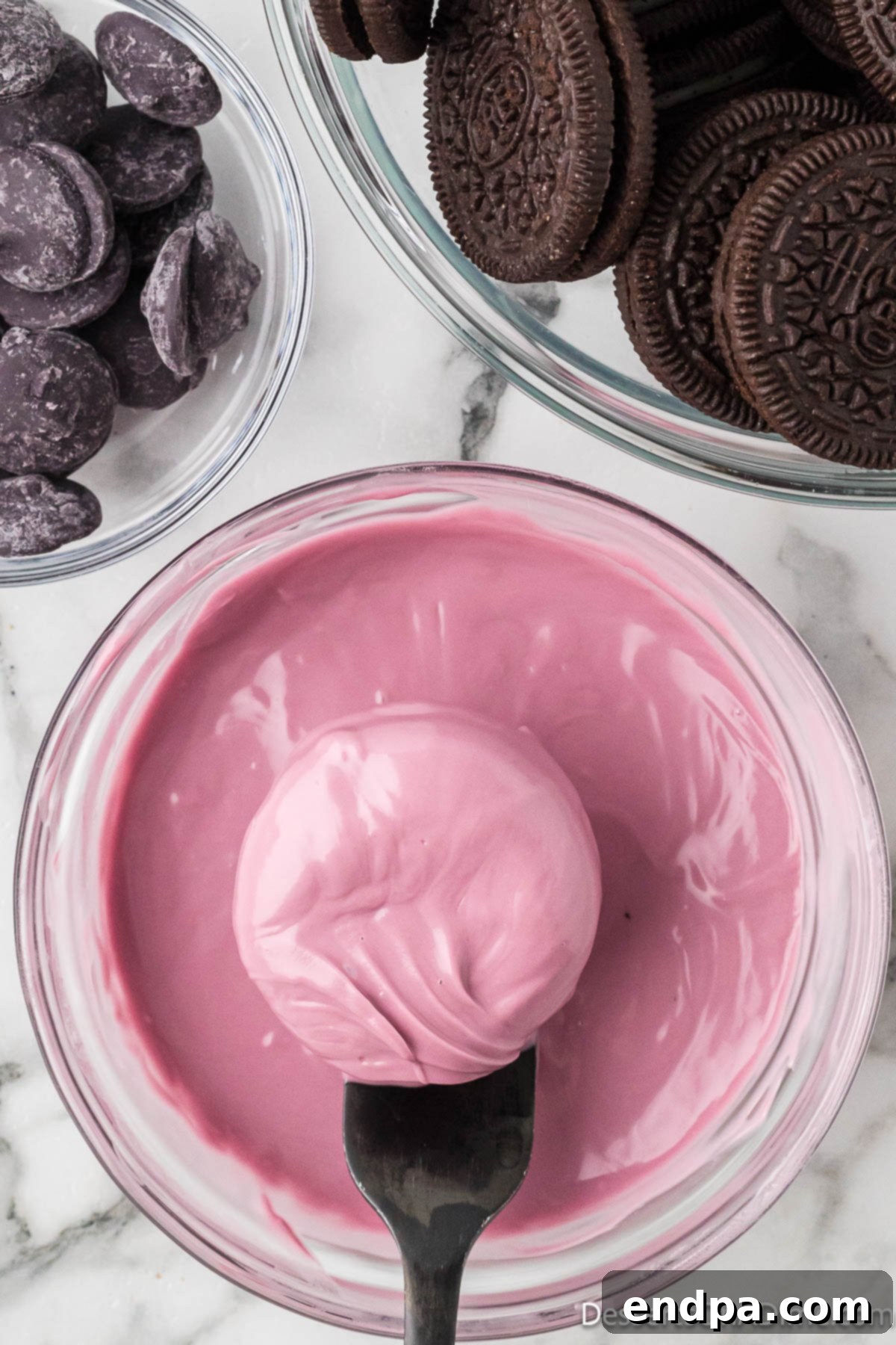 An Oreo cookie, freshly dipped in purple candy melts, being gently tapped to remove excess coating.